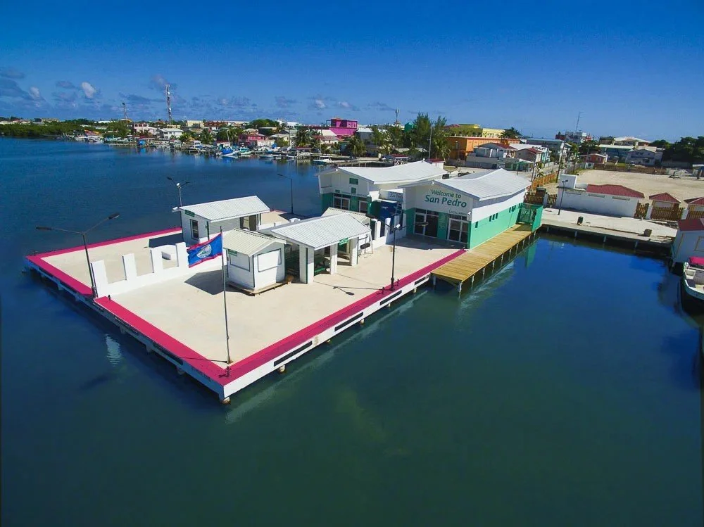 Aerial view of a waterfront building with a pier in San Pedro, featuring a modern structure with a sign that reads "Welcome to San Pedro."