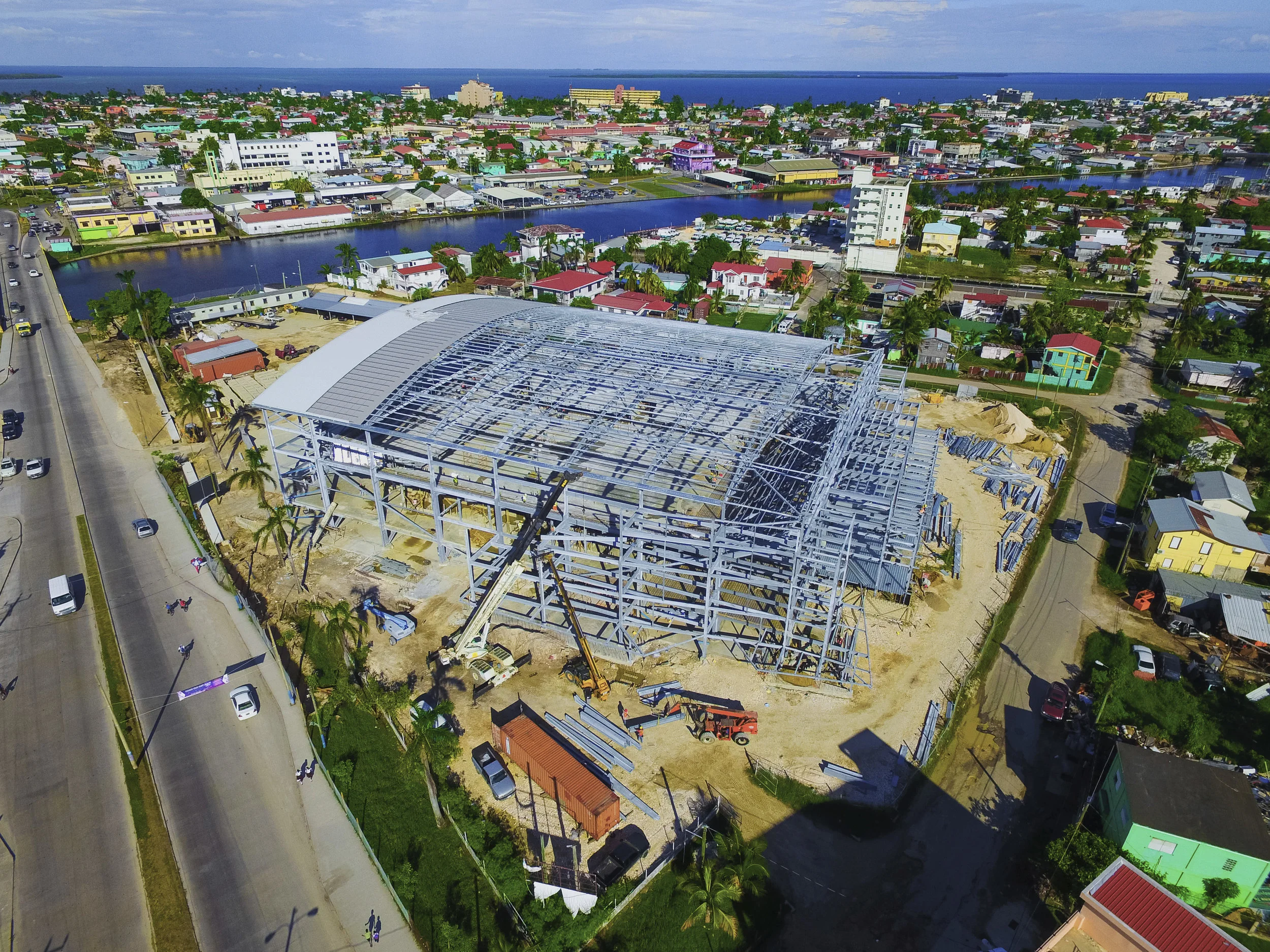 Aerial view of a tropical cityscape with a waterway, colorful houses, tall buildings, and an under-construction large structure.