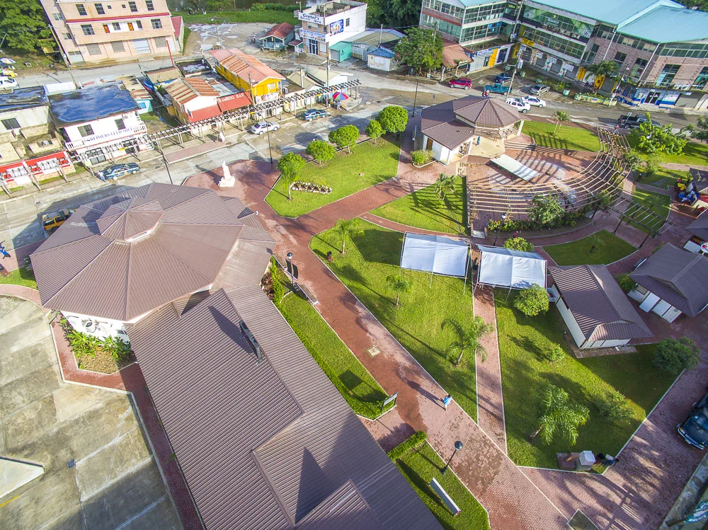 Aerial view of a park with walkways, green lawns, small trees, a gazebo, outdoor stages, and surrounding buildings.