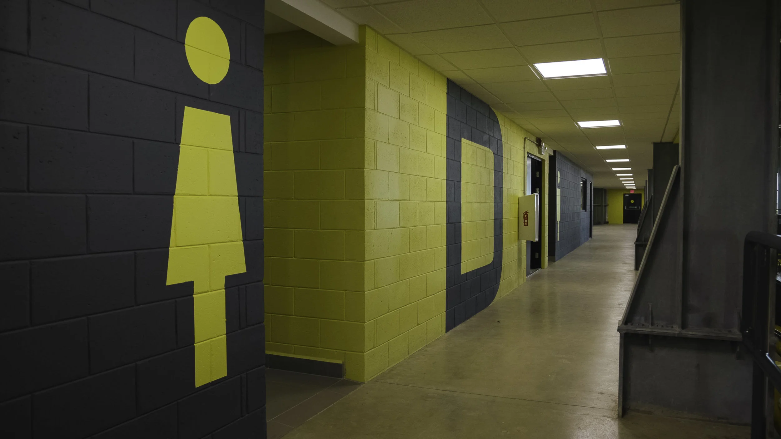 A hallway with dark and yellow painted brick walls, featuring large yellow dollar signs, and illuminated ceiling lights.