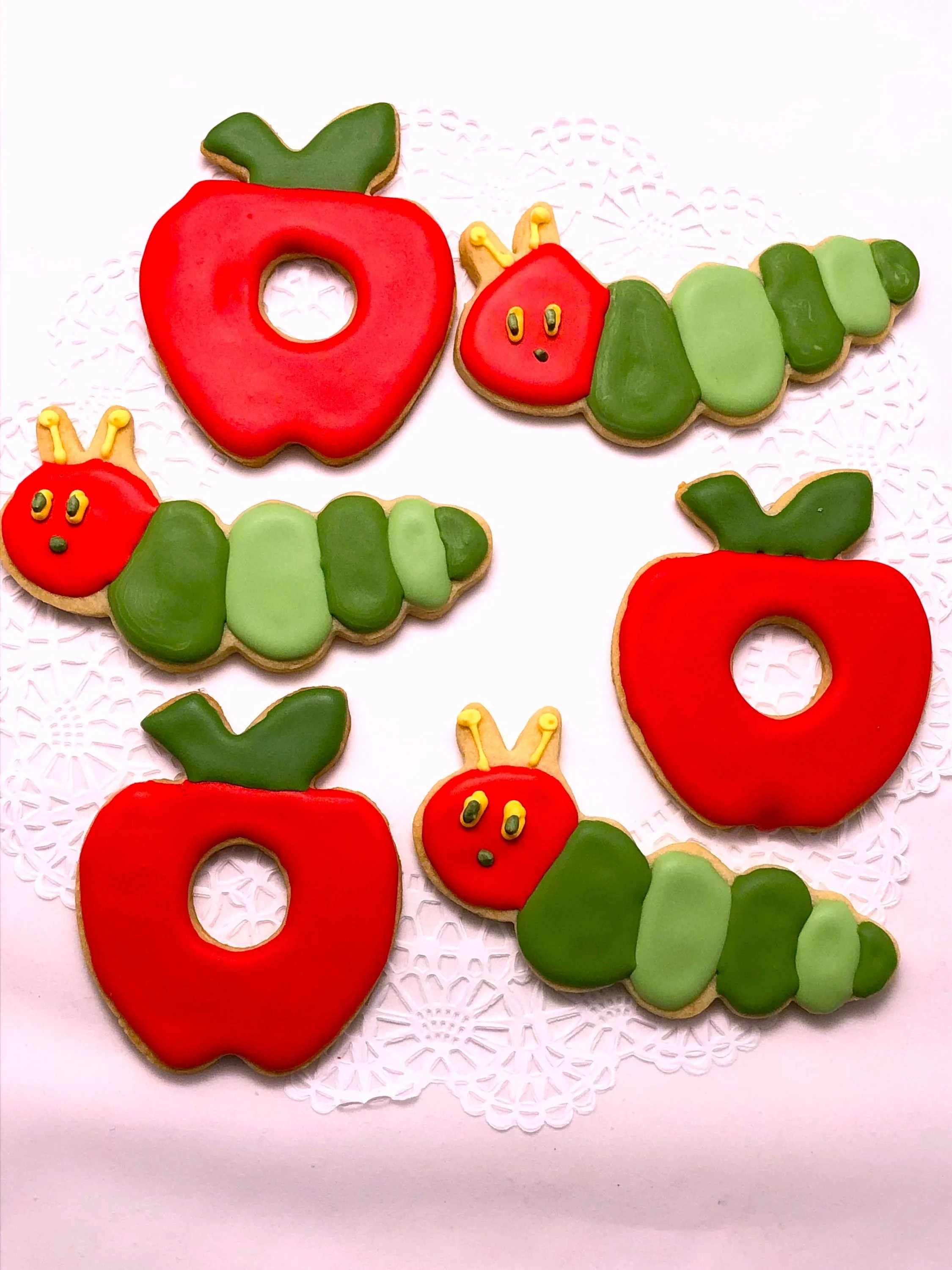 Very Hungry Caterpillar themed cut-out cookies decorated with colorful caterpillar and apple designs