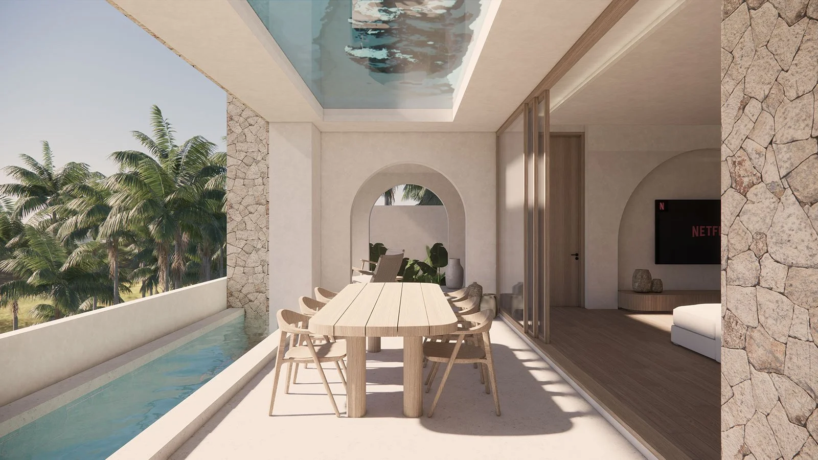 Open-air balcony with a long wooden dining table and seven chairs, overlooking palm trees and a pool, with sliding glass doors leading to a living room with a flat-screen TV.