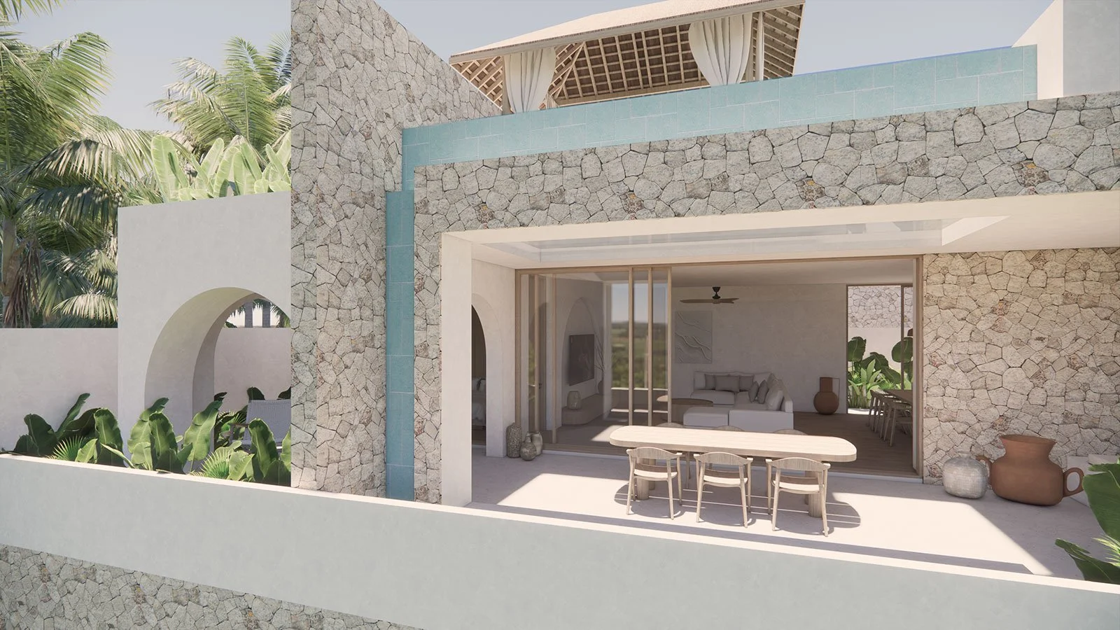 Modern outdoor patio with stone walls, glass sliding doors, a dining table with chairs, and a living area with a couch and artwork inside, surrounded by greenery and tropical plants.