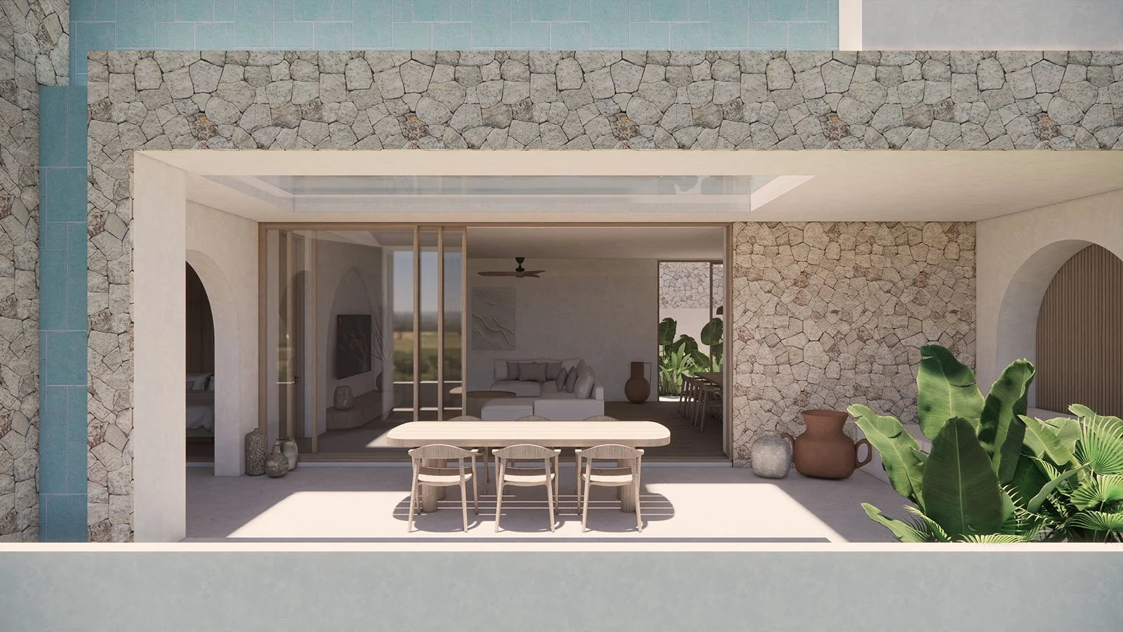 Outdoor patio with a wooden dining table and four chairs, rocky wall, large green plants, two large pottery vases, and view into a modern living room with a white sofa and a ceiling fan.