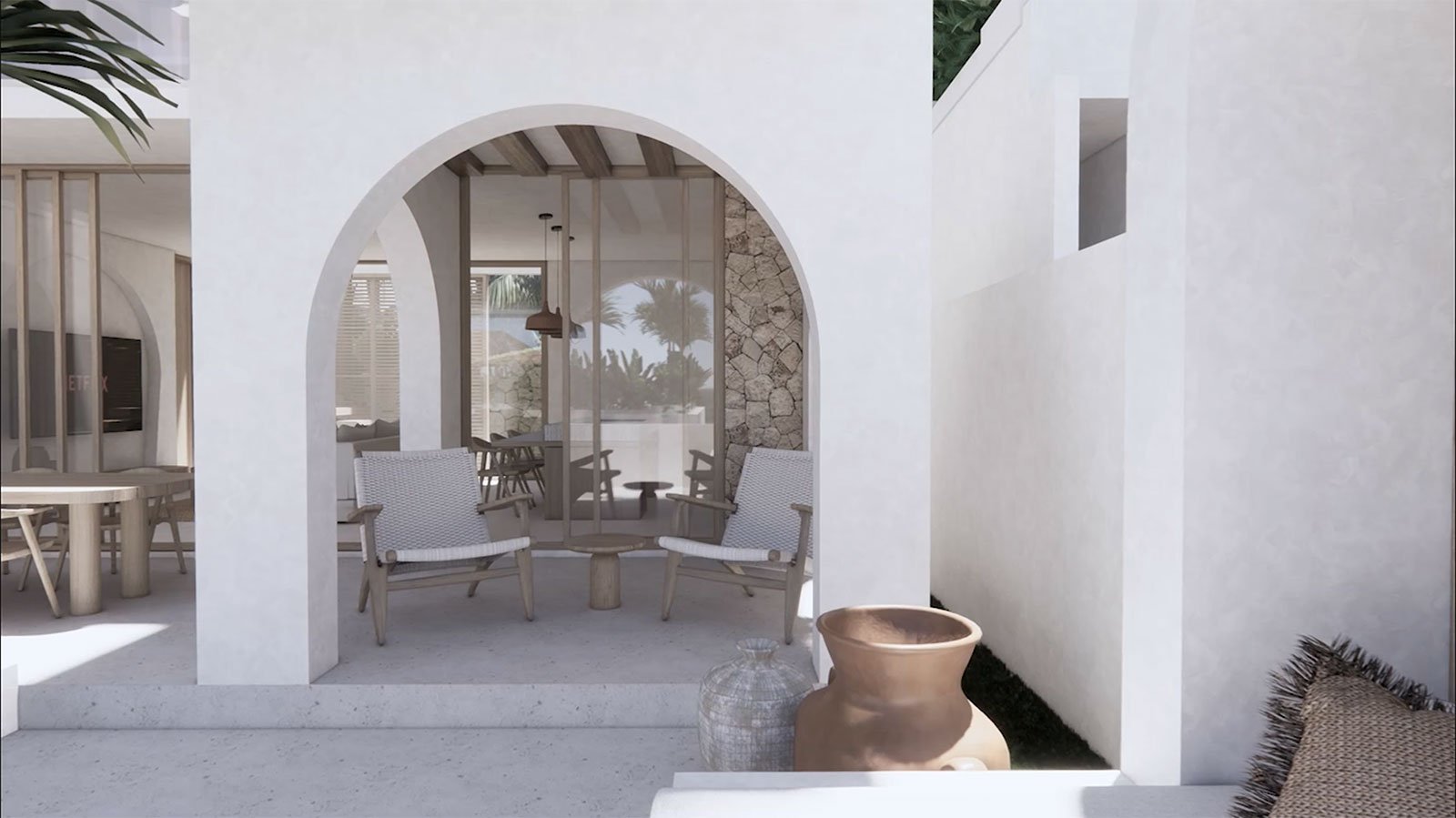 Outdoor patio area with white walls, arched openings, two wooden chairs with woven seats, a small round table, decorative vases, and tropical plants visible through glass doors.