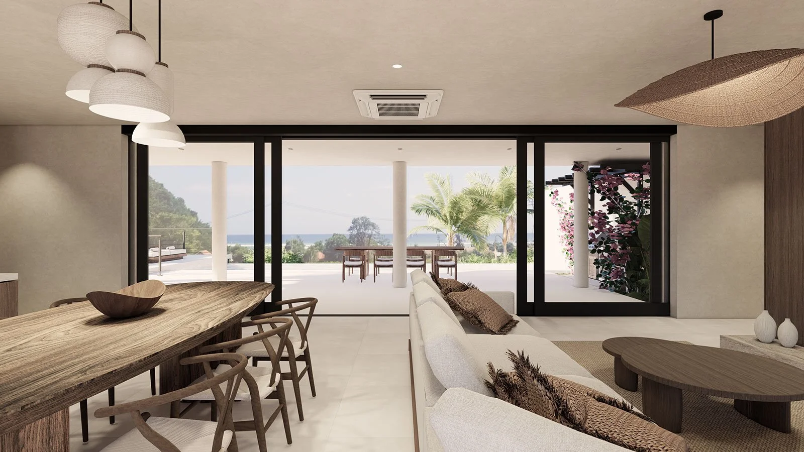 Living room with large glass sliding doors opening to a patio with outdoor dining, tropical trees, and ocean view, decorated in neutral tones with wooden furniture.