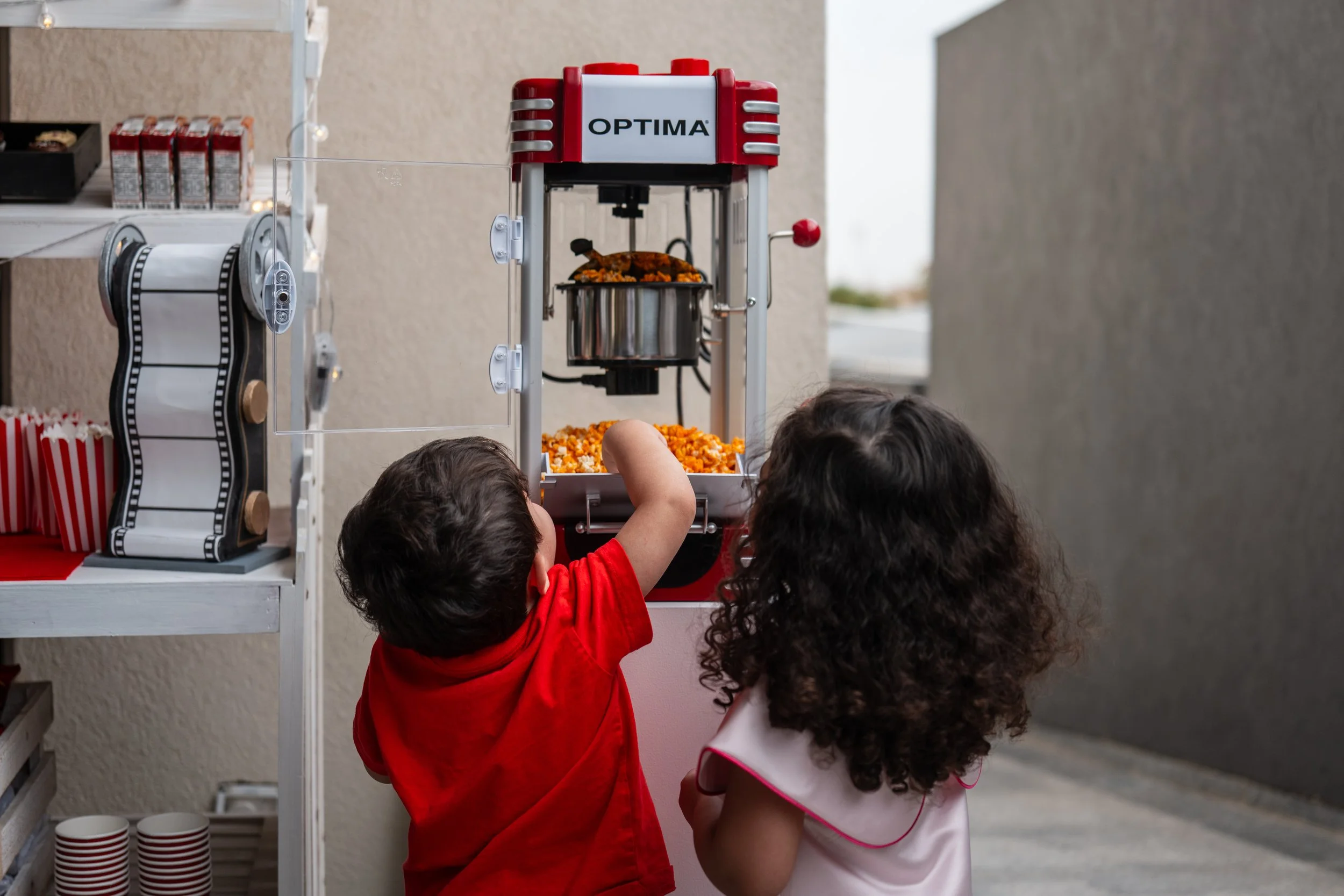 Two children, a boy and a girl, sharing popcorn from a vending machine outside.