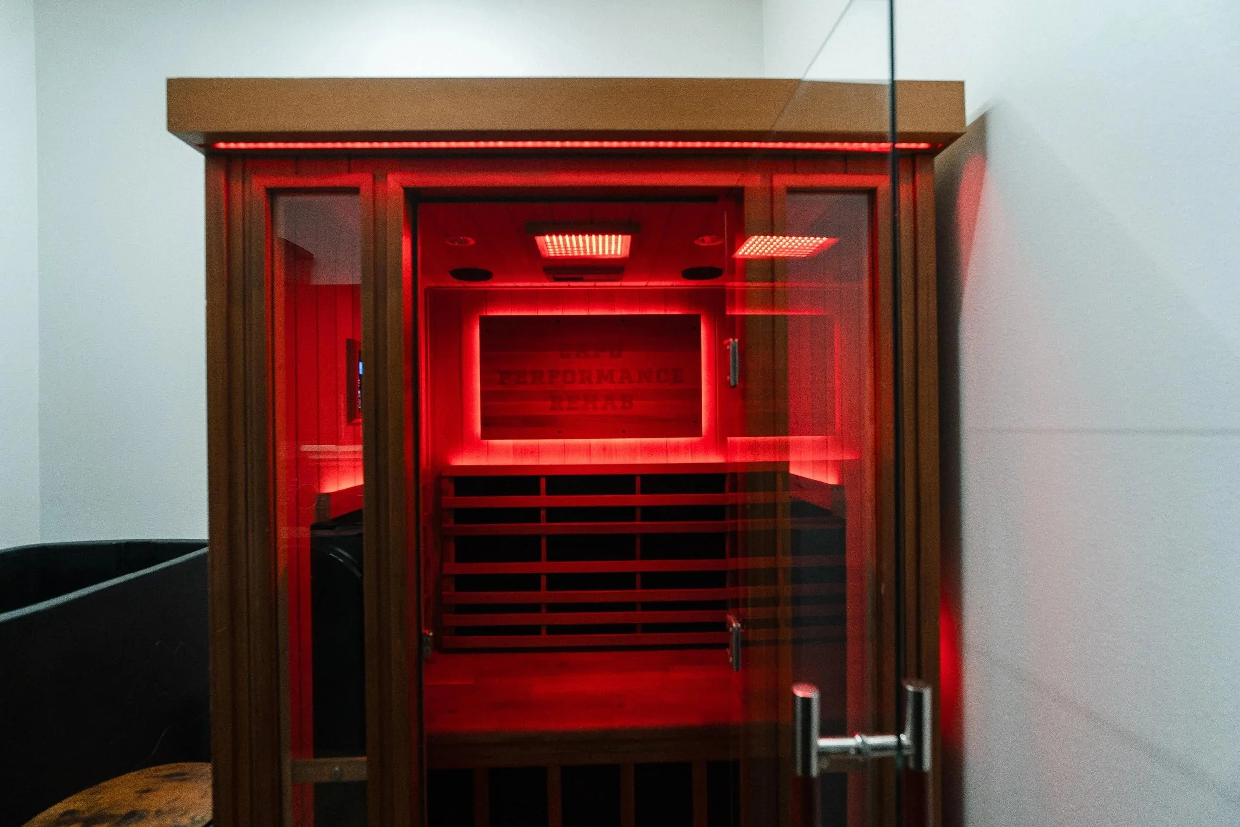 A wooden sauna with glass door and red interior lighting, with the words "Performance" visible inside.