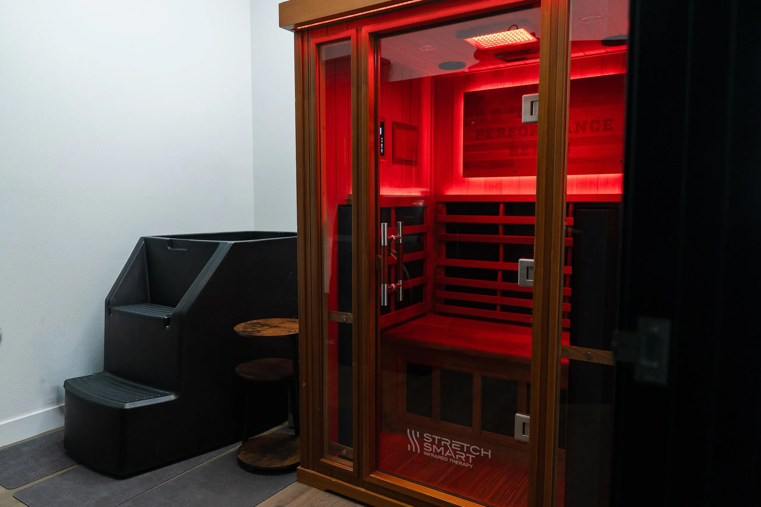 Infrared therapy sauna with wooden frame in a room, next to cold plunge and small table, in a medical or wellness facility.