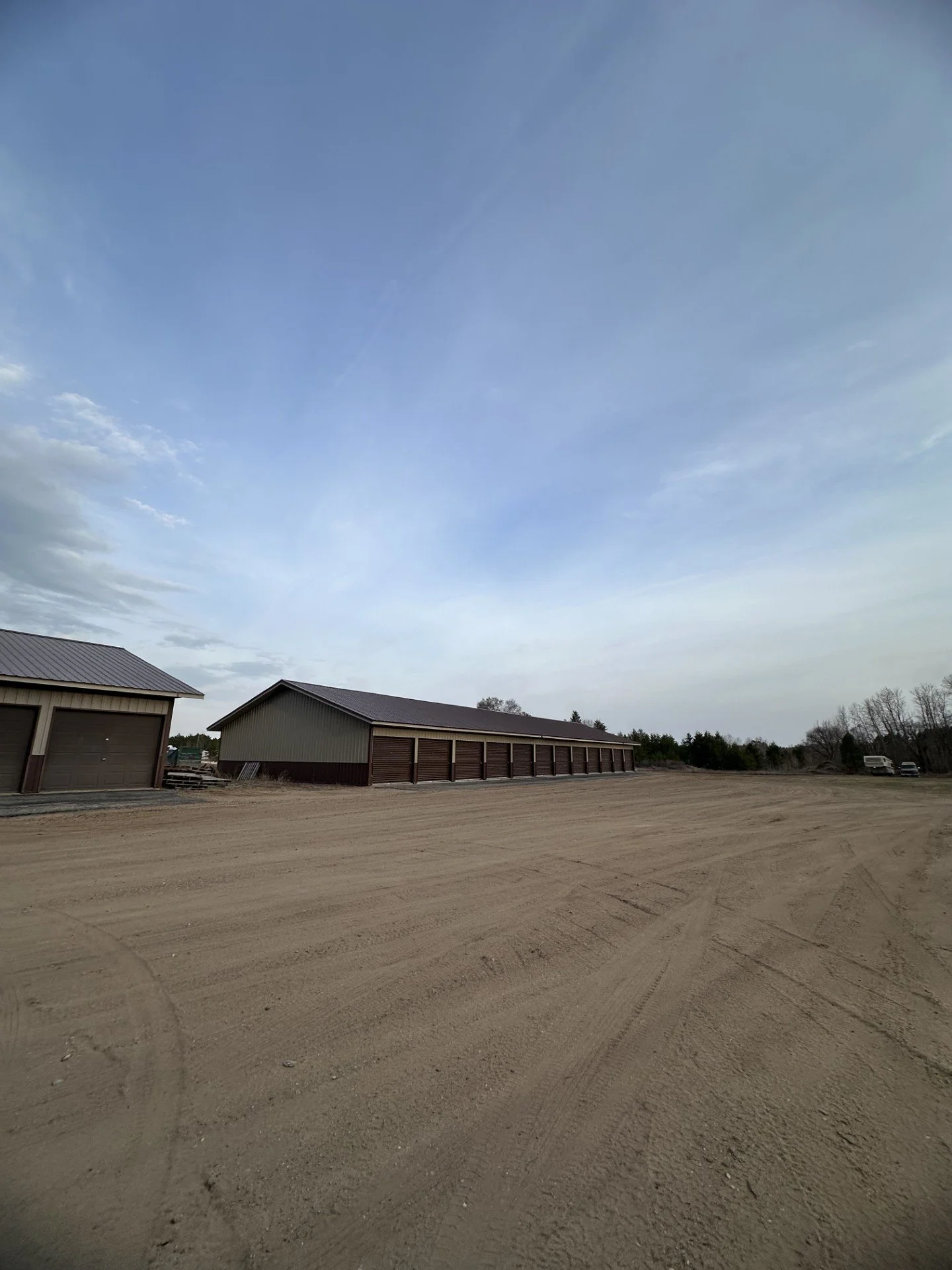 A wide view of a dirt lot with large storage buildings and a cloudy sky.