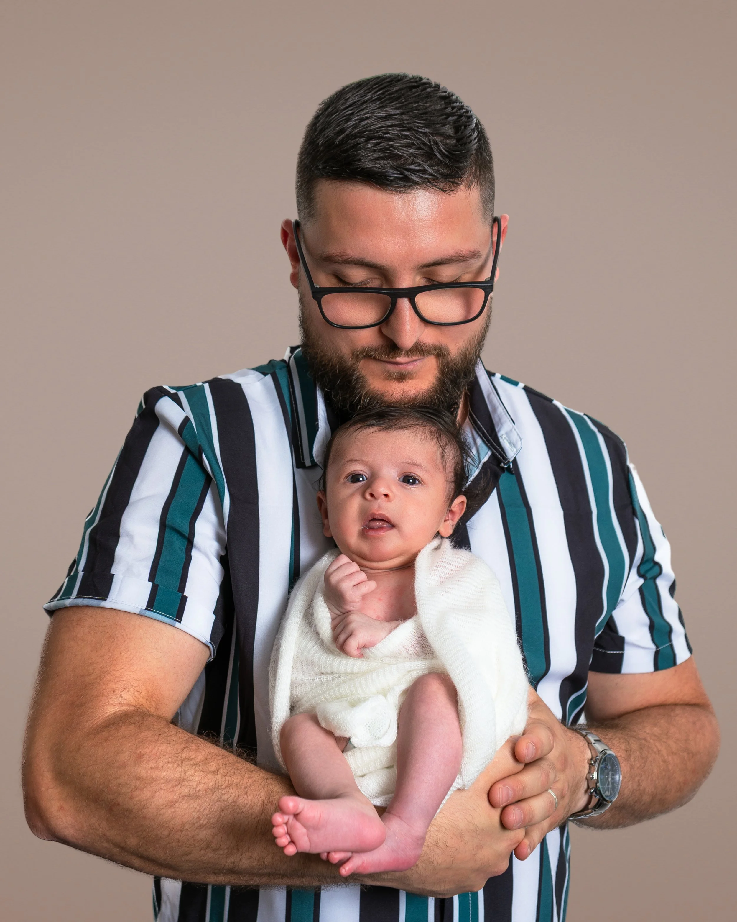 A man with glasses and a beard holding a baby in his arms, both with their eyes closed in a calm moment.