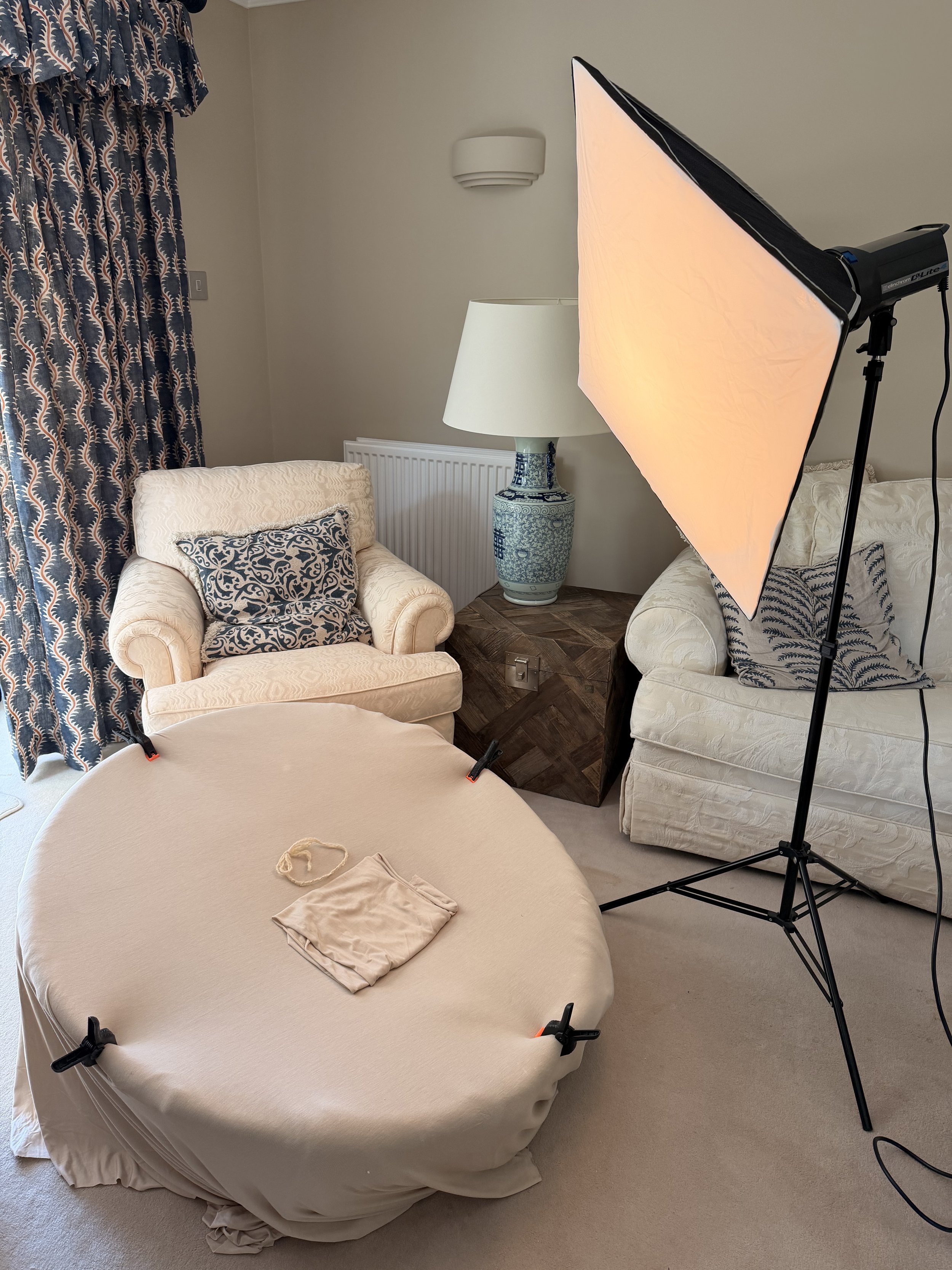 A living room with two armchairs, a side table, lamp, blue and white patterned curtains, and a professional lighting setup.