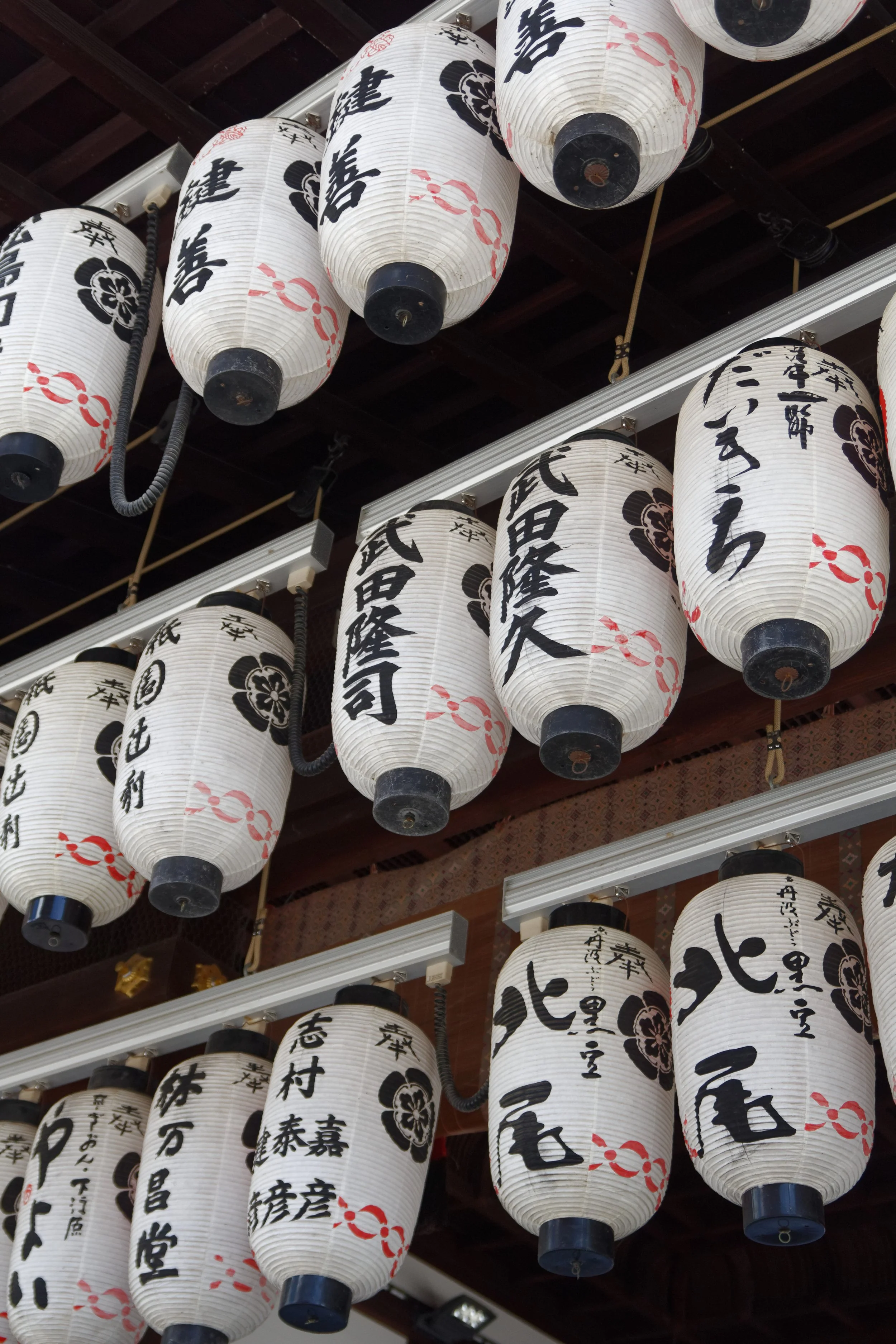 Littérature japonaise traditionnelle avec des lanternes en papier blanc suspendues, décorées de caractères kanji noirs et de motifs floraux noirs.