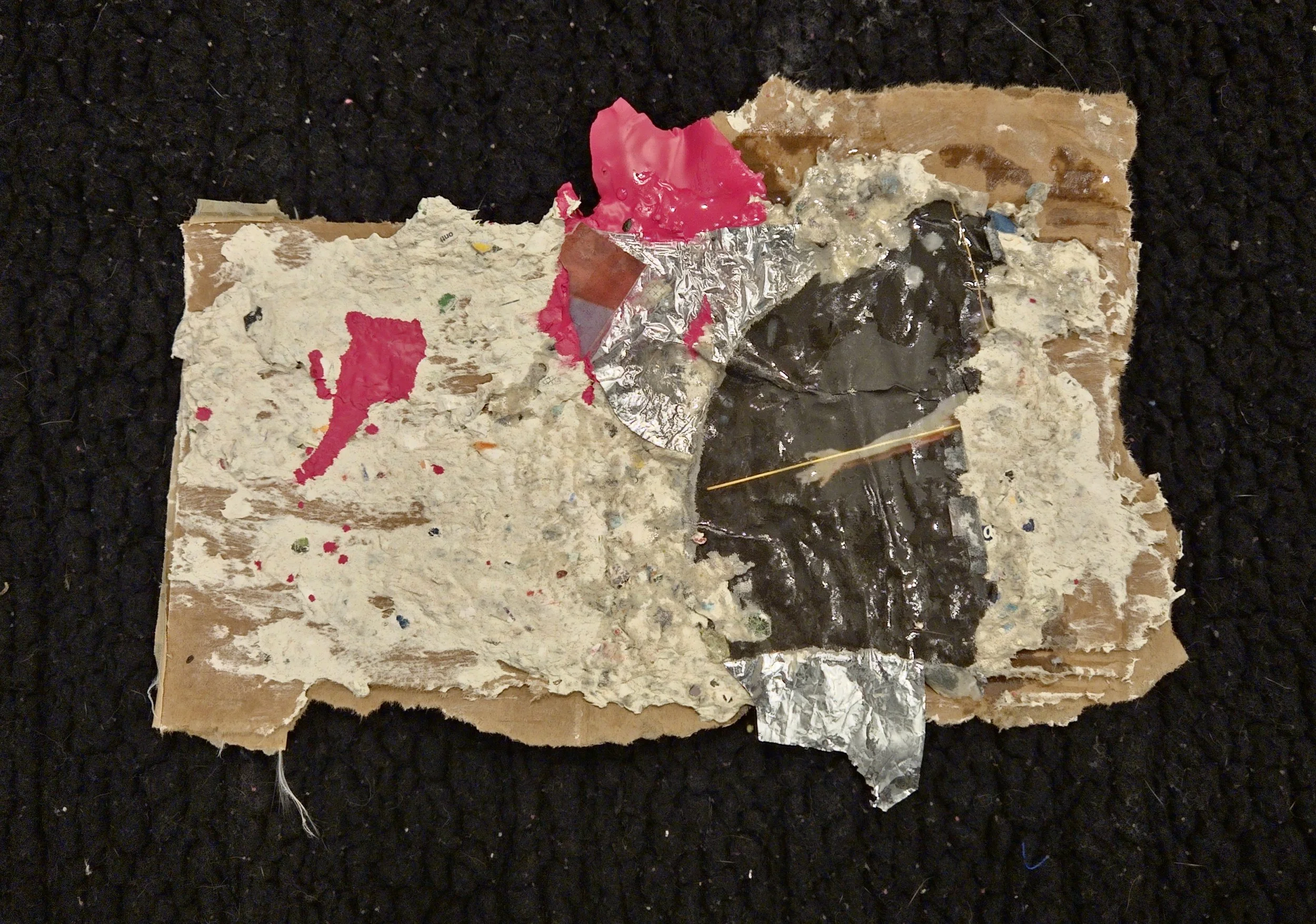 Torn, stained, and crumpled pieces of paper, tape, and foil on a dark fabric background.