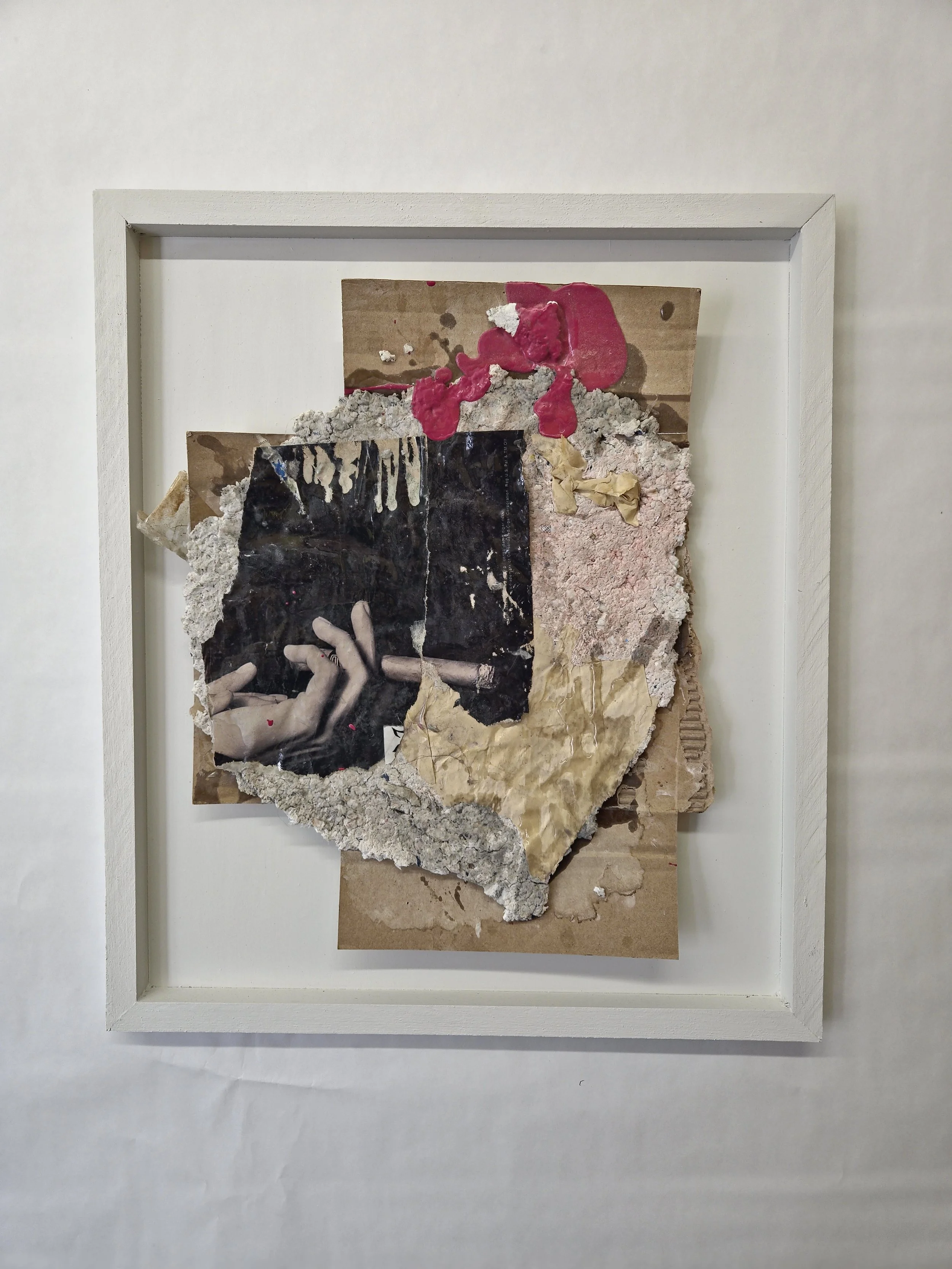 Mixed media artwork with torn paper, a black photograph of a hand holding a cigarette, and various textured and colored paper layers framed in a white shadow box.