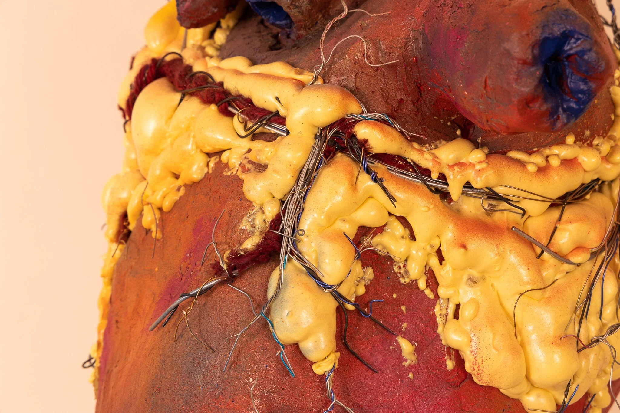 A close-up of a medical or artistic sculpture showing exposed flesh, wires, and yellow substance resembling tissue or foam.