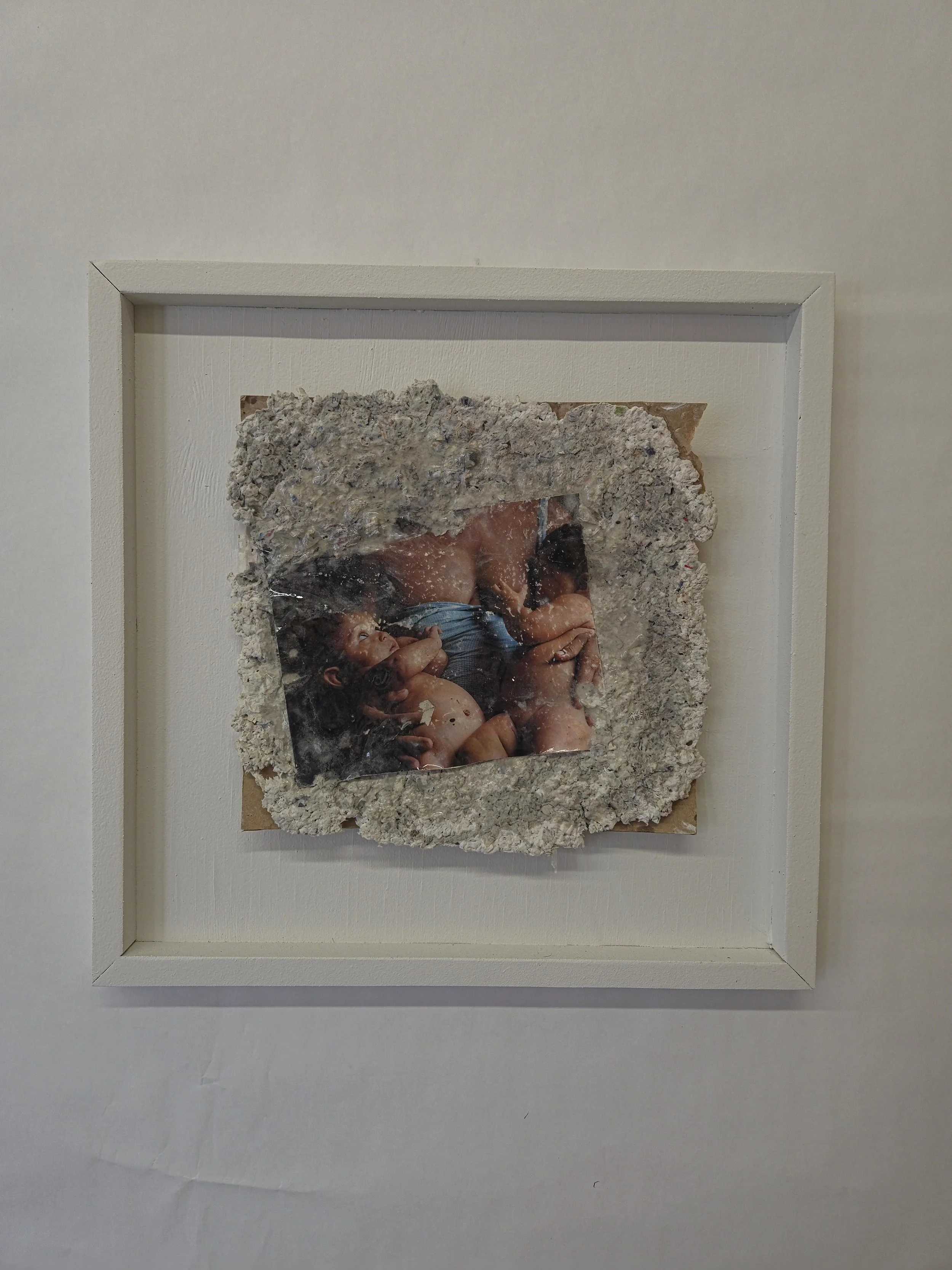 Mixed media artwork featuring a photograph of people lying together, framed with rough concrete-like material on white background.
