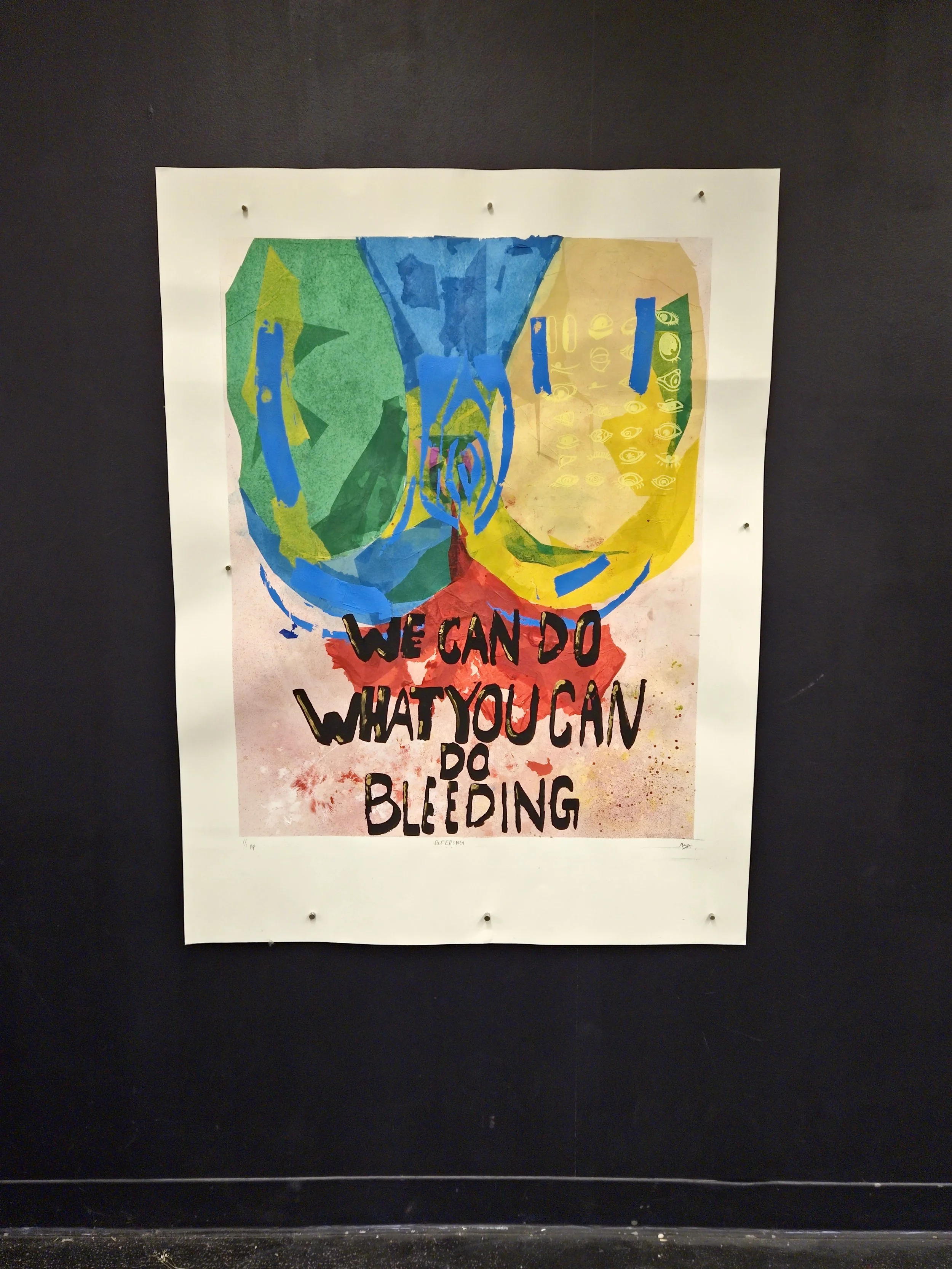 Colorful abstract artwork with the text 'We can do what you can do bleeding' written across it, displayed on a black wall.