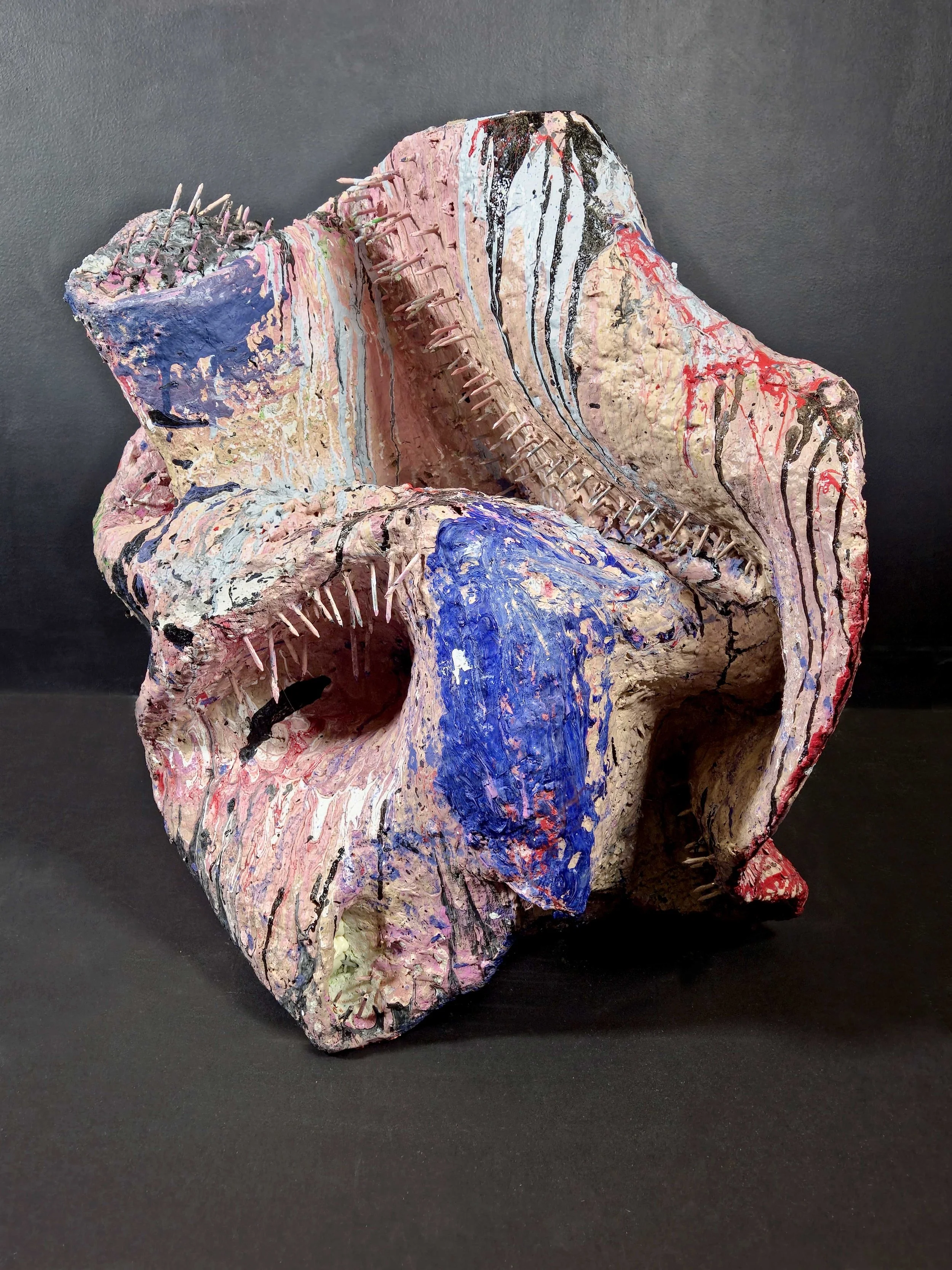 Abstract mixed-media sculpture with textured, colorful paint layers, spike details, and a black background.