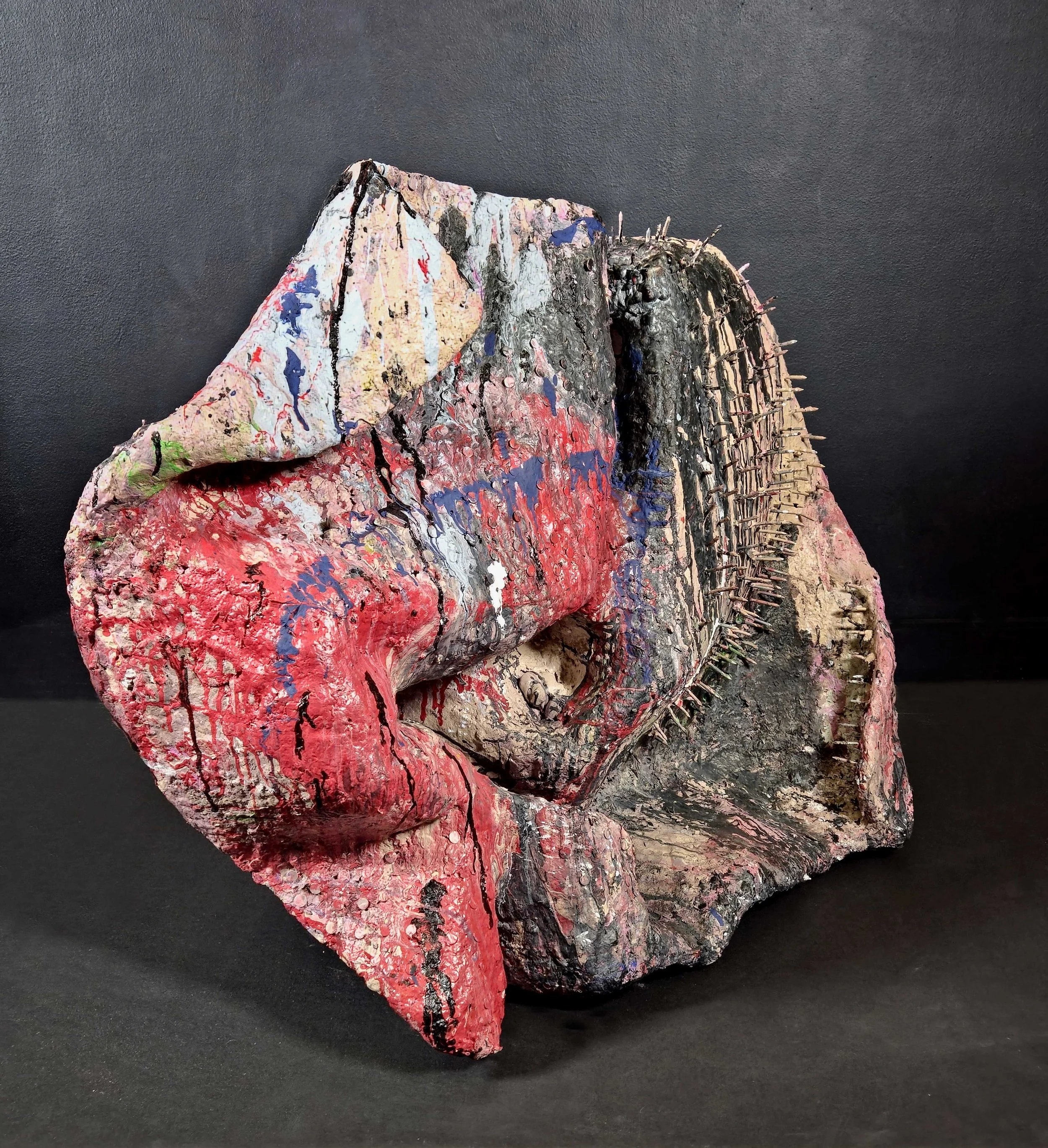 Mixed media abstract sculpture resembling a hand forming a fist with textured, painted, and embedded elements, set against a black background.