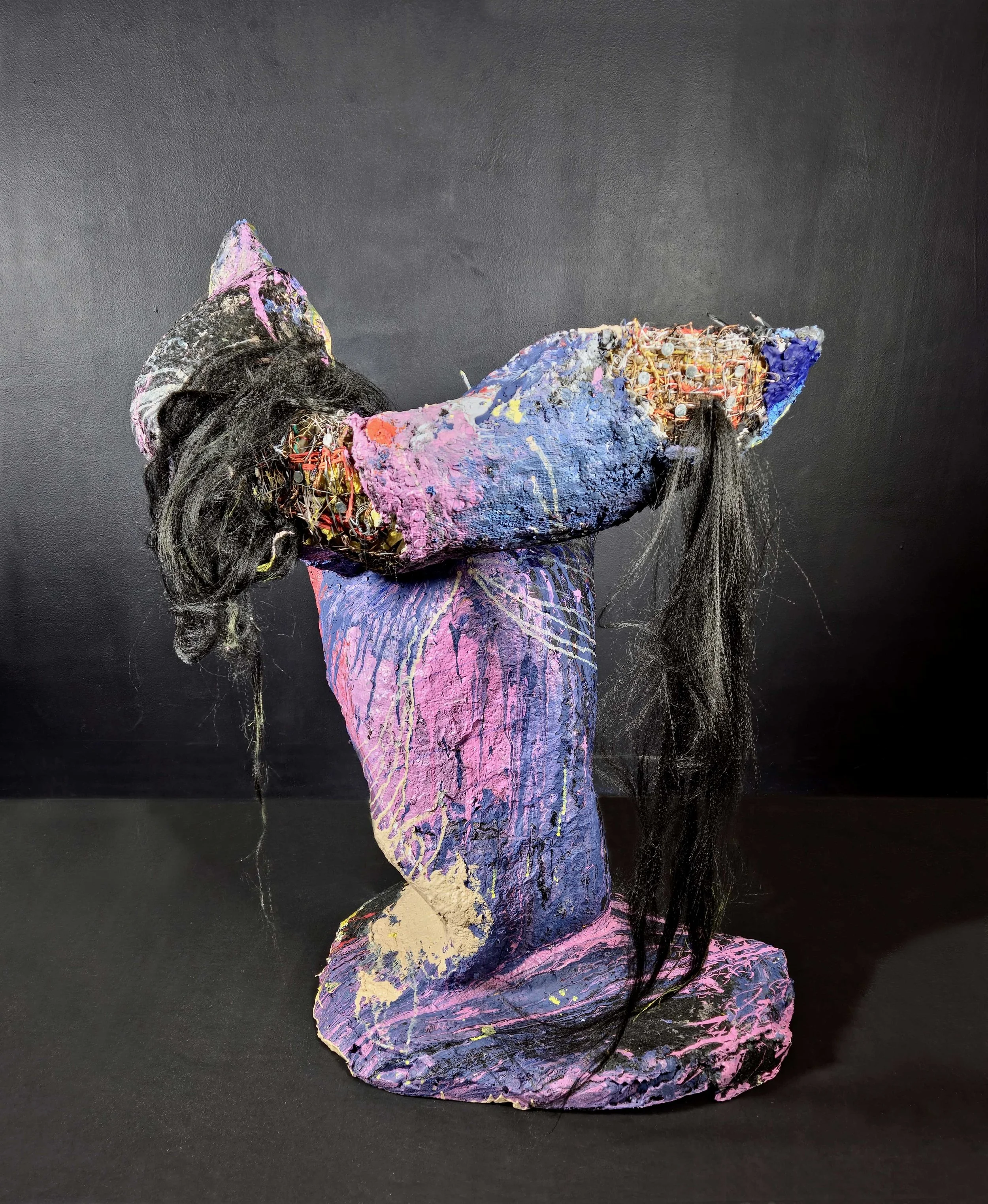 Mixed media sculpture of a woman with long black hair, painted in shades of pink and purple, against a black background.