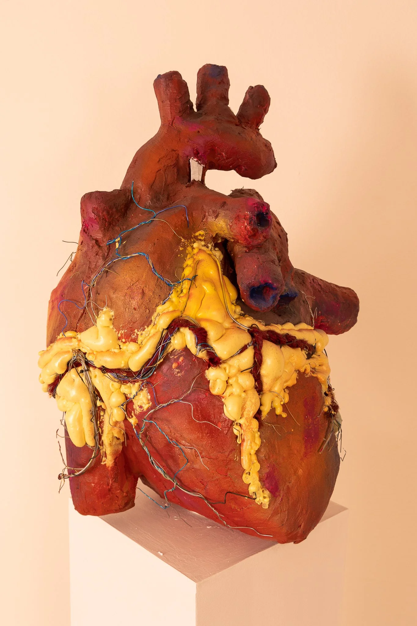 An art piece resembling a human heart, made with mixed media including clay, wires, and foam, displayed on a pedestal against a plain background.