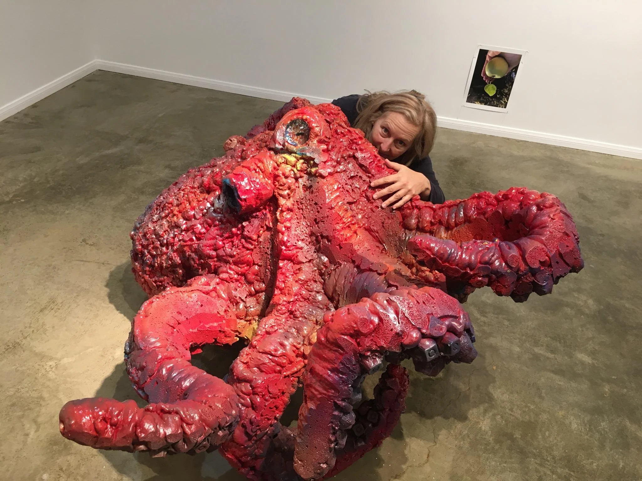 Woman hugging a large, textured red octopus sculpture in an art gallery.