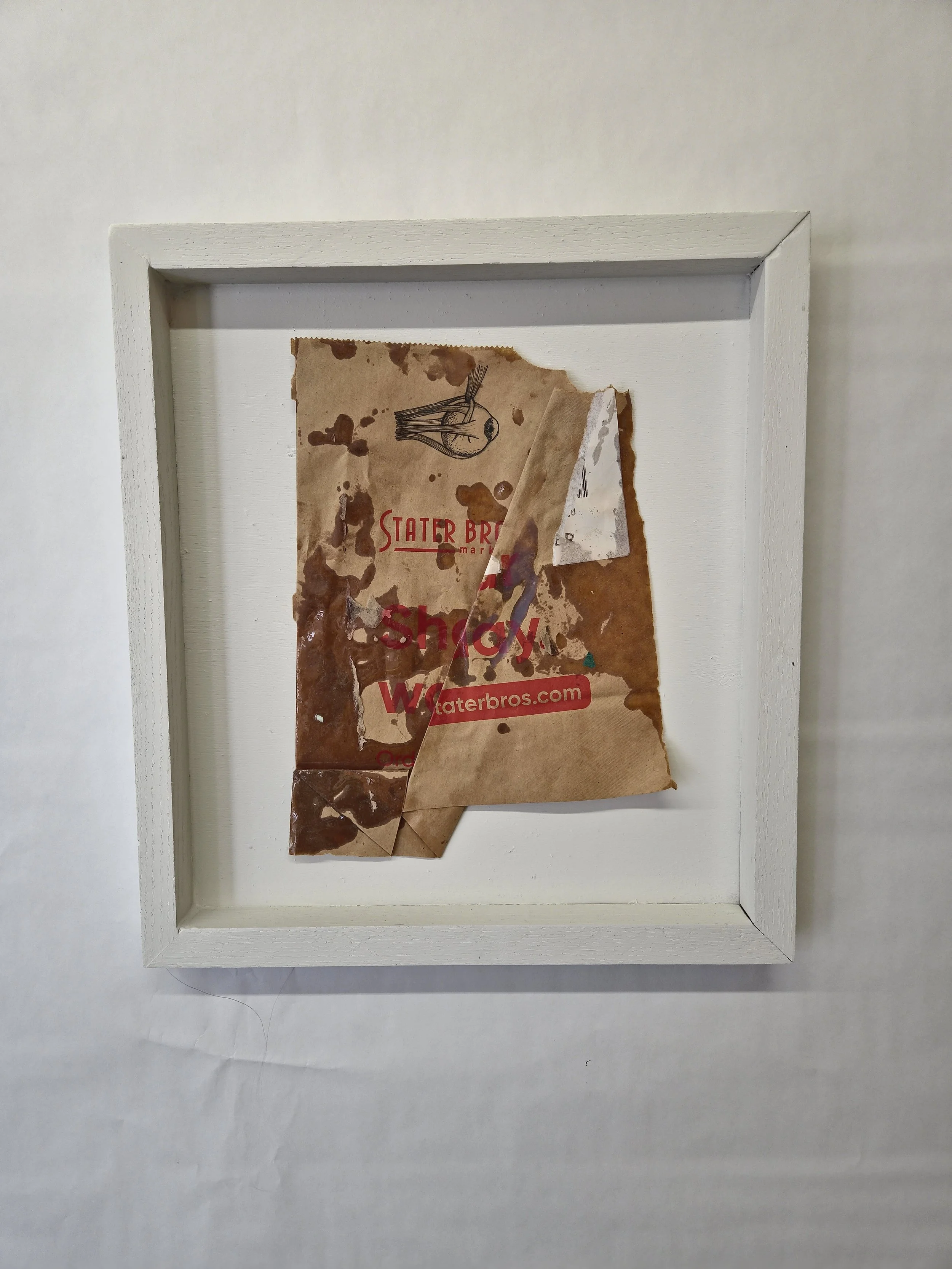 Framed, aged, torn paper from a Water Bros brand bag with a sketch of a fish and the text 'Shore' and 'waterbros.com' on a white background.