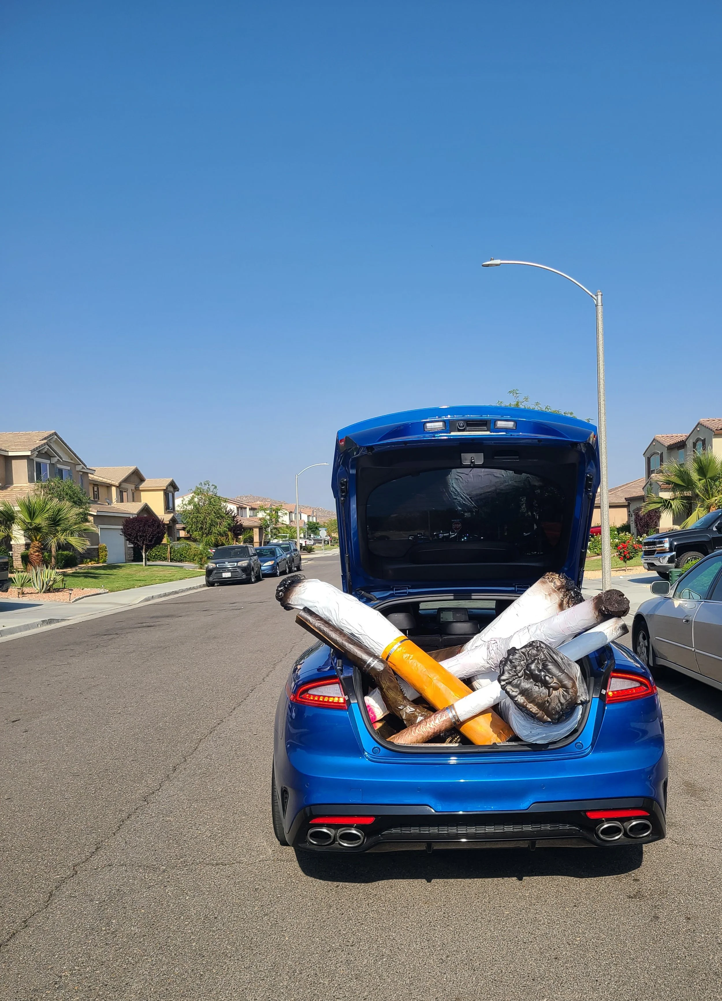 A blue car with its trunk open filled with large, unlit cigars.