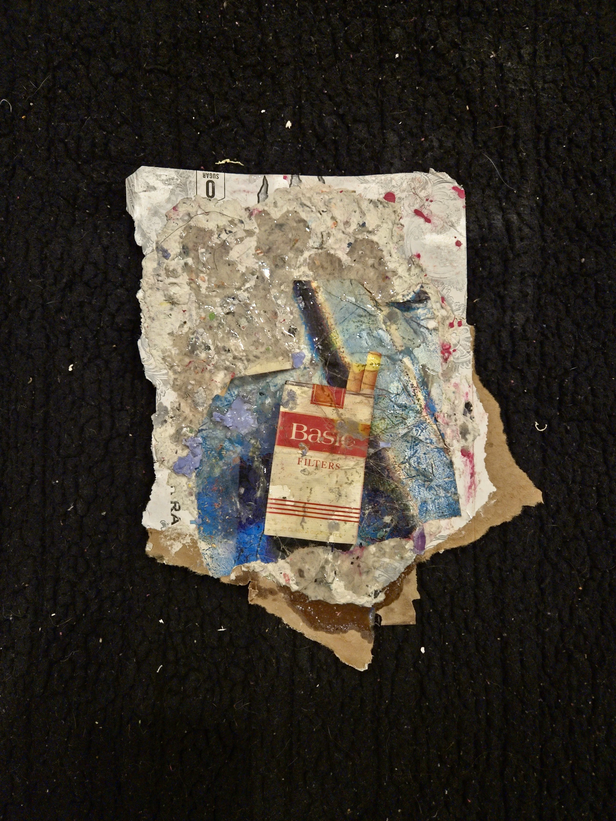 A burned, crumpled piece of paper with smudges, ink, and remnants of a colorful graphic, including a partially visible red and white box labeled 'Basic Filters,' lying on a black textured surface.