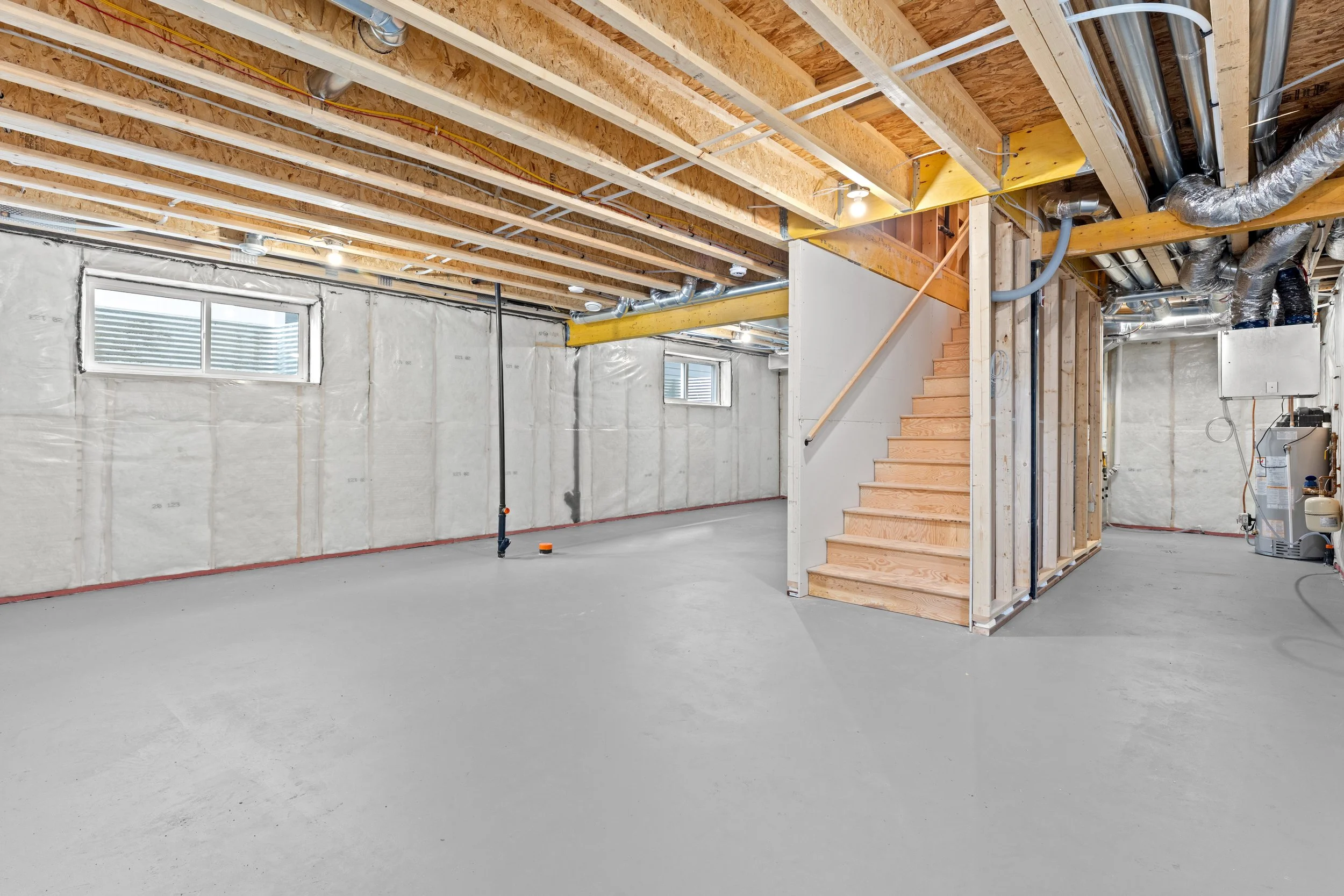 Unfinished basement under renovation featuring continuous foundation insulation, egress window well, and exposed joist framing.