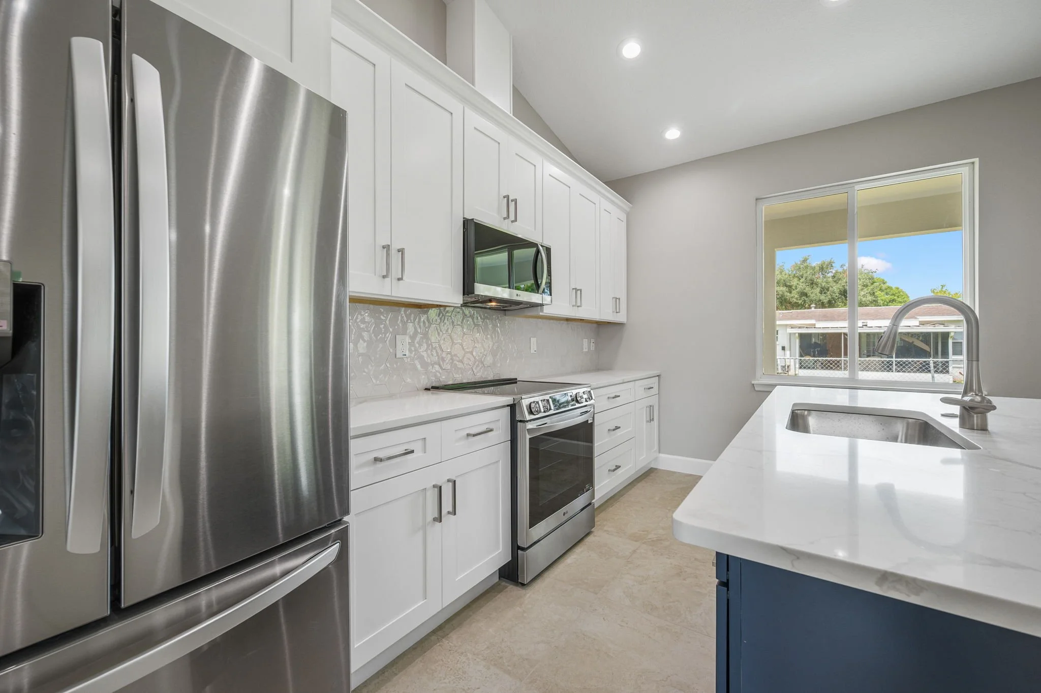 Modern kitchen with white cabinets, stainless steel appliances, a large window, and a white countertop with a built-in sink.