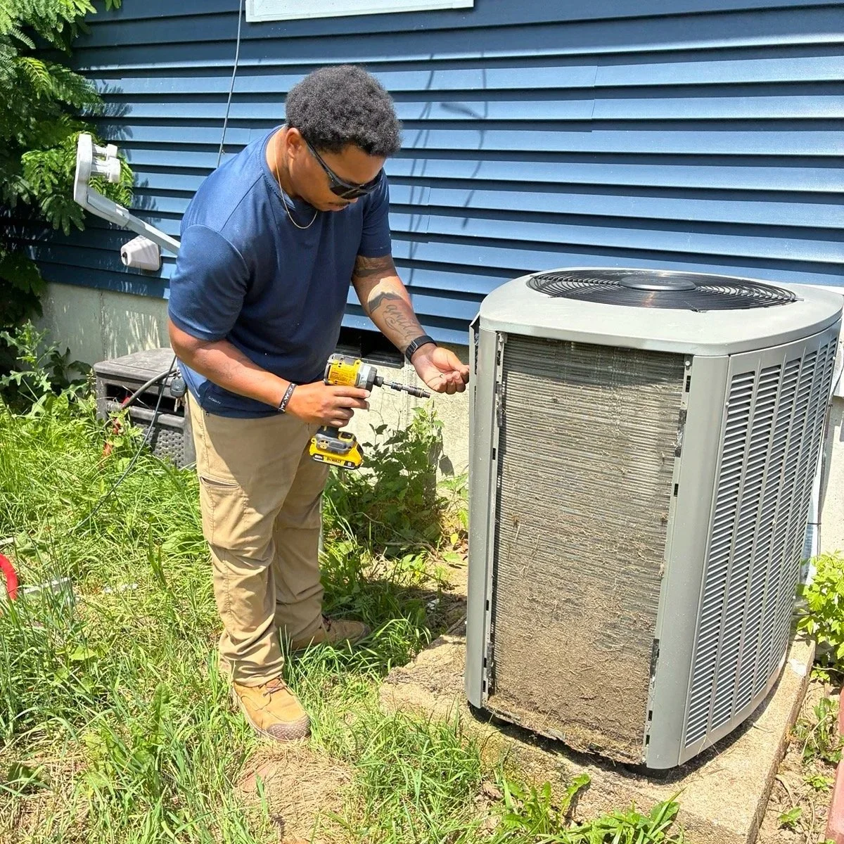 A man repairing an outdoor air conditioning unit with a power drill.