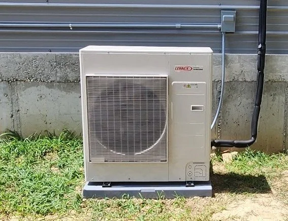 Outdoor Lennox air conditioning unit on a concrete pad next to a house with grass in front.