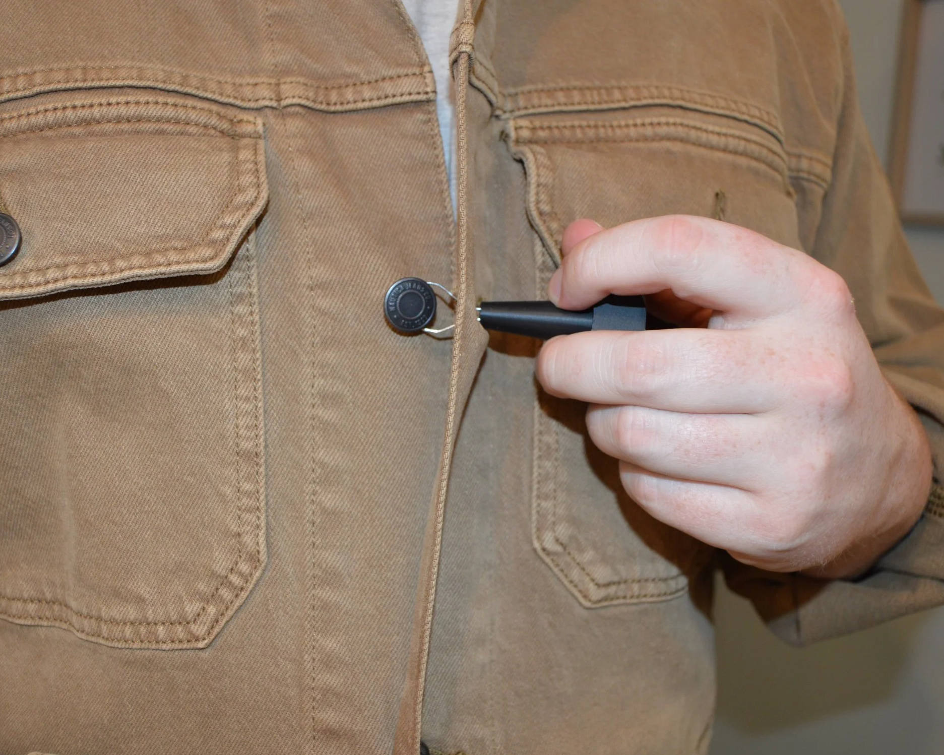 Close-up of a person in a brown jacket buttoning the top button of their jacket.