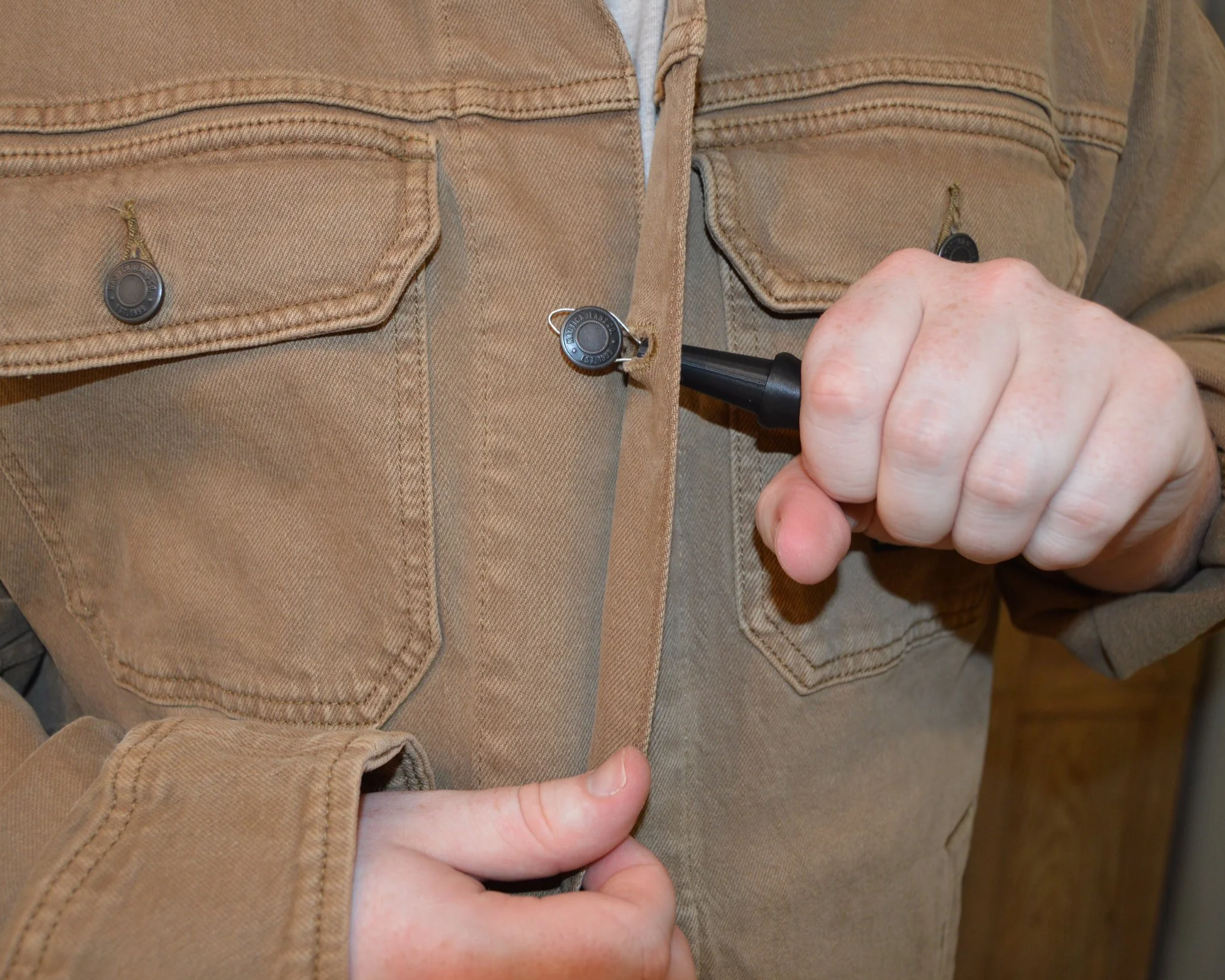 Close-up of a person fastening a button on a tan-colored jacket with one hand.