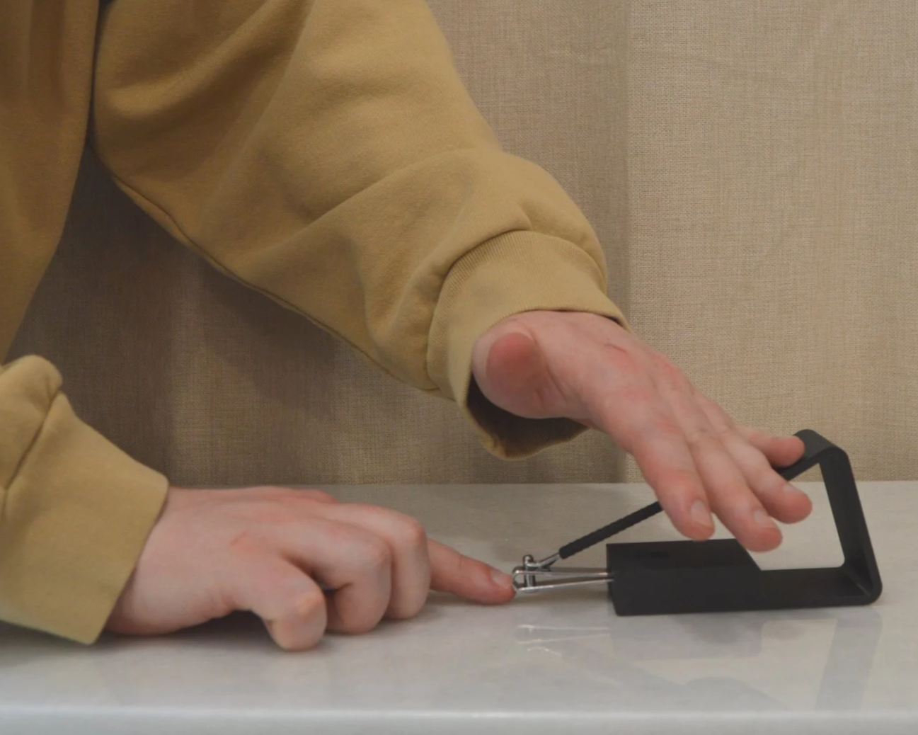 Person in a yellow sweatshirt demonstrating a wire hanger trap on a surface, with their right hand pressing down on the trap and their left hand steadying it.
