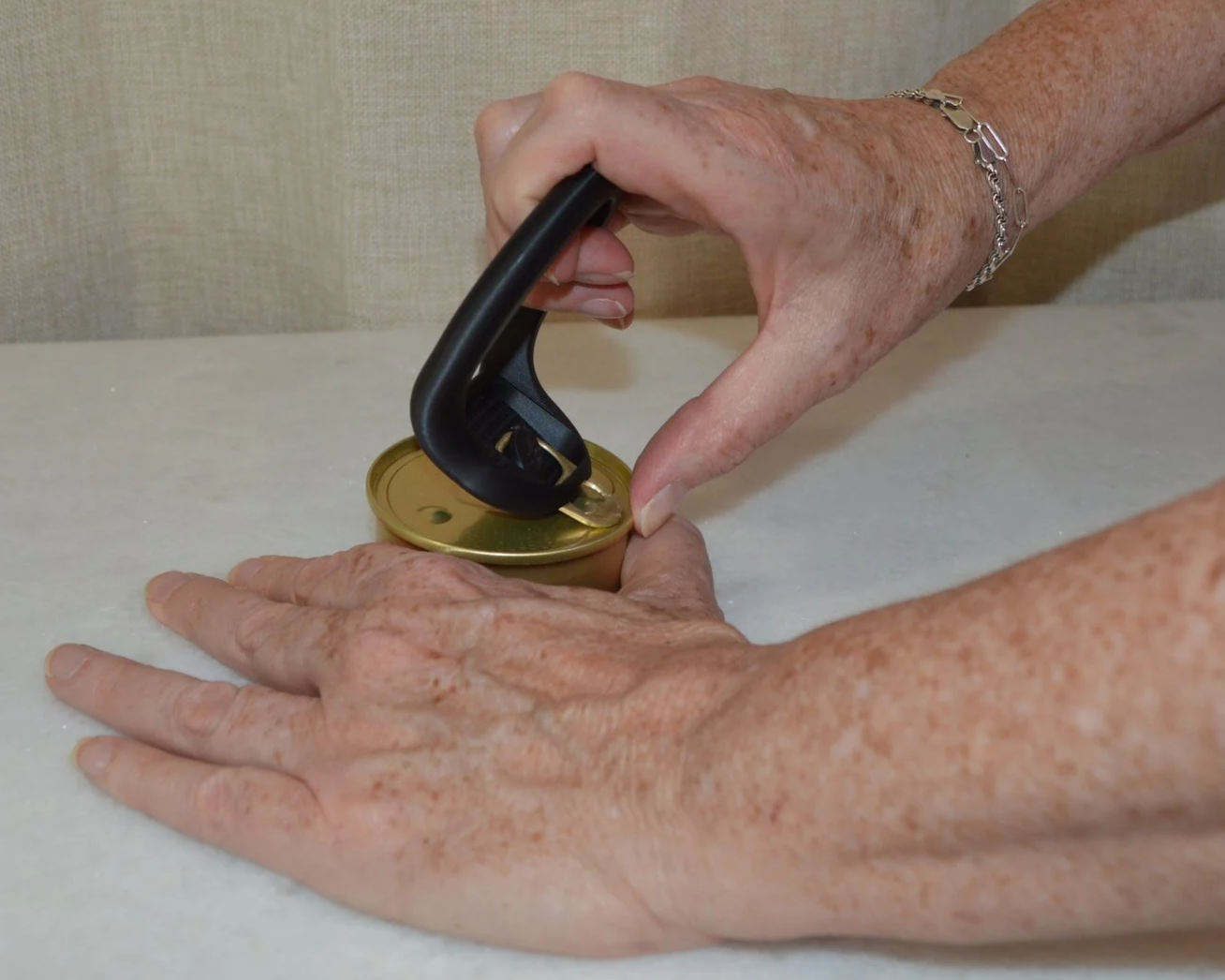 A person using a can opener to open a jar on a light-colored surface.