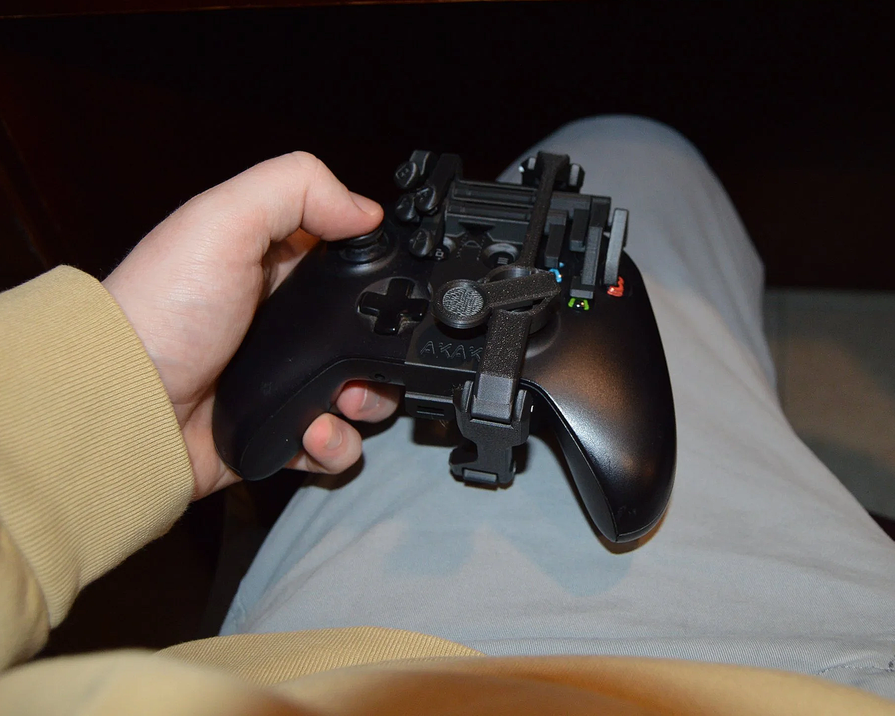 A person wearing a beige long-sleeve shirt holding a black gaming controller with a phone holder attachment mounted on it.