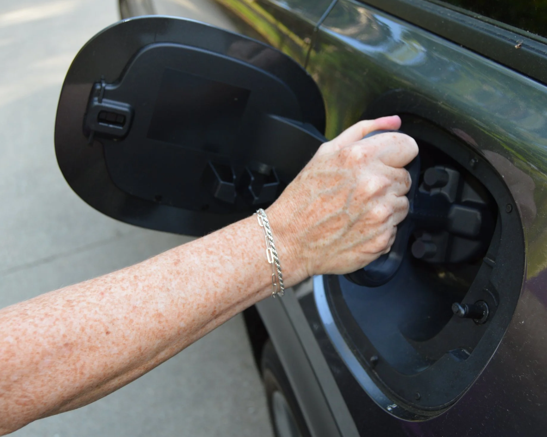 A person filling up a black electric vehicle with a charging cable outdoors.