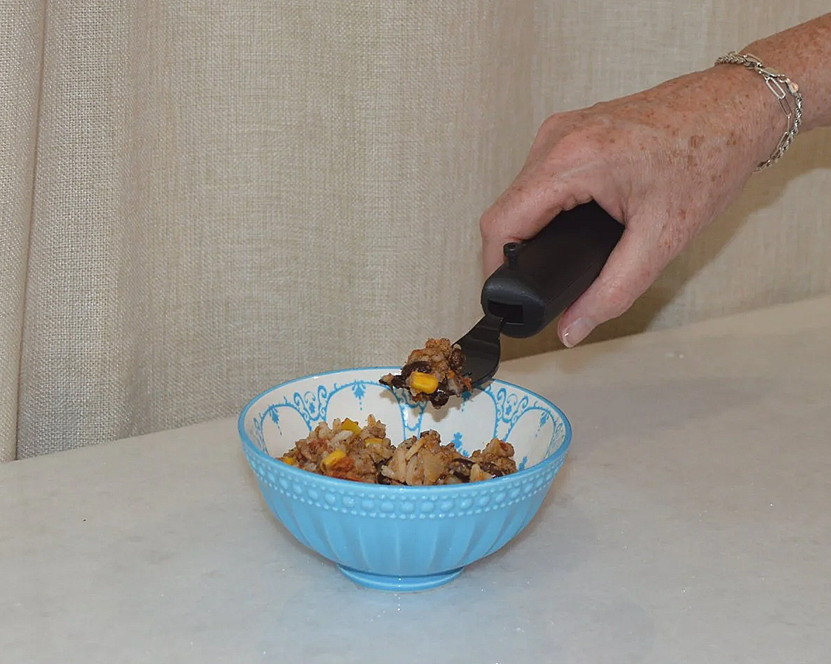 Elderly hand scooping a portion of beef and vegetable stew from a blue patterned bowl with a black serving utensil.