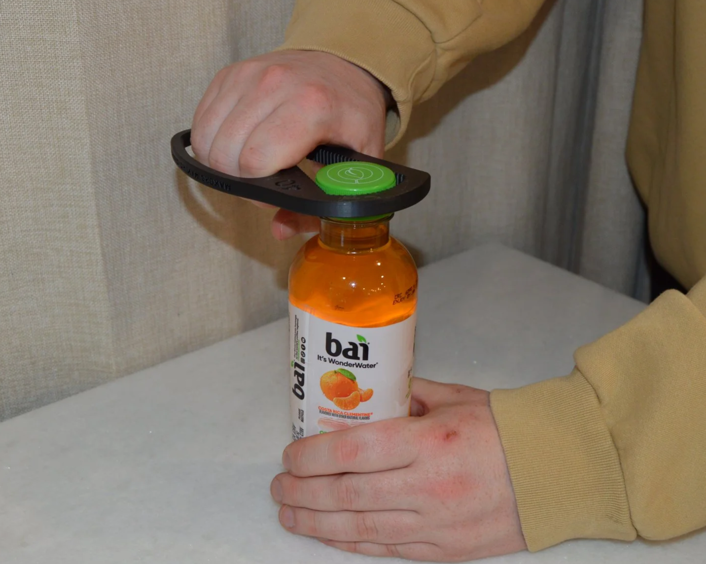 Person's hands opening a bottle of Bai orange-flavored antioxidant drink with a bottle opener.