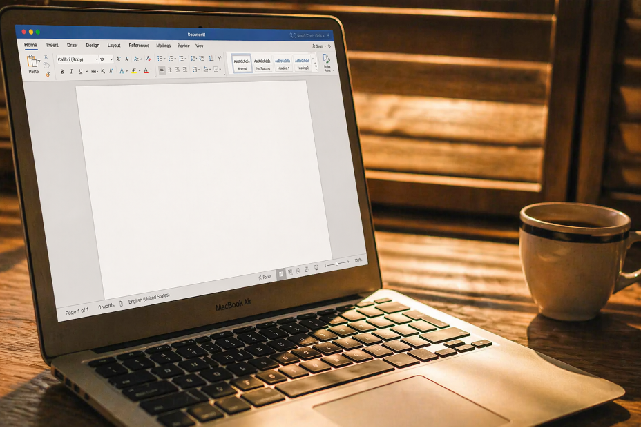An open MacBook Air on a wooden table with a blank document on the screen and a cup of coffee nearby.