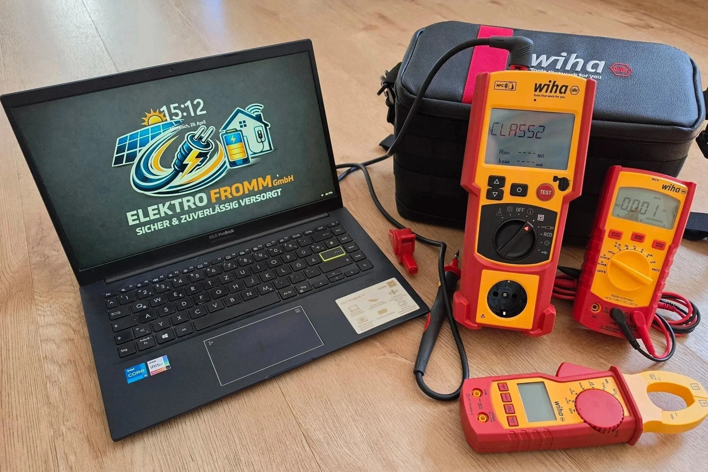 Laptop auf einem Holztisch mit Messgeräten und Werkzeugen für elektrische Messungen, darunter ein Multimeter, im Hintergrund eine schwarze Tasche. Der Laptop zeigt das Logo einer Elektrofachfirma.