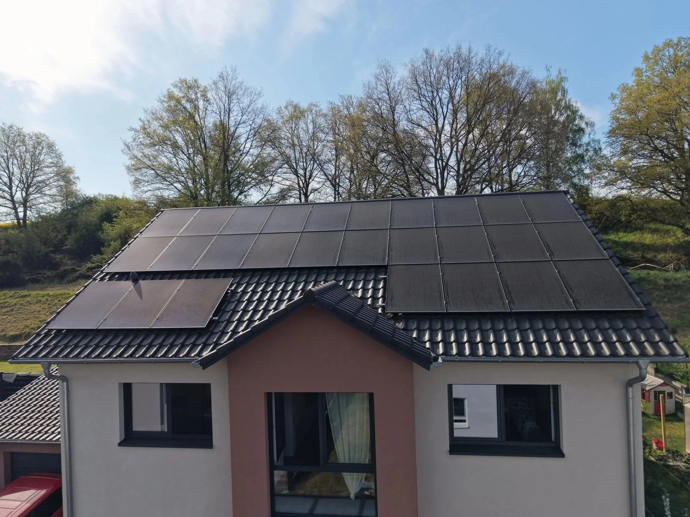 Ein Haus mit Solarpanelen auf dem Dach, umgeben von Bäumen und im Hintergrund ein blauer Himmel
