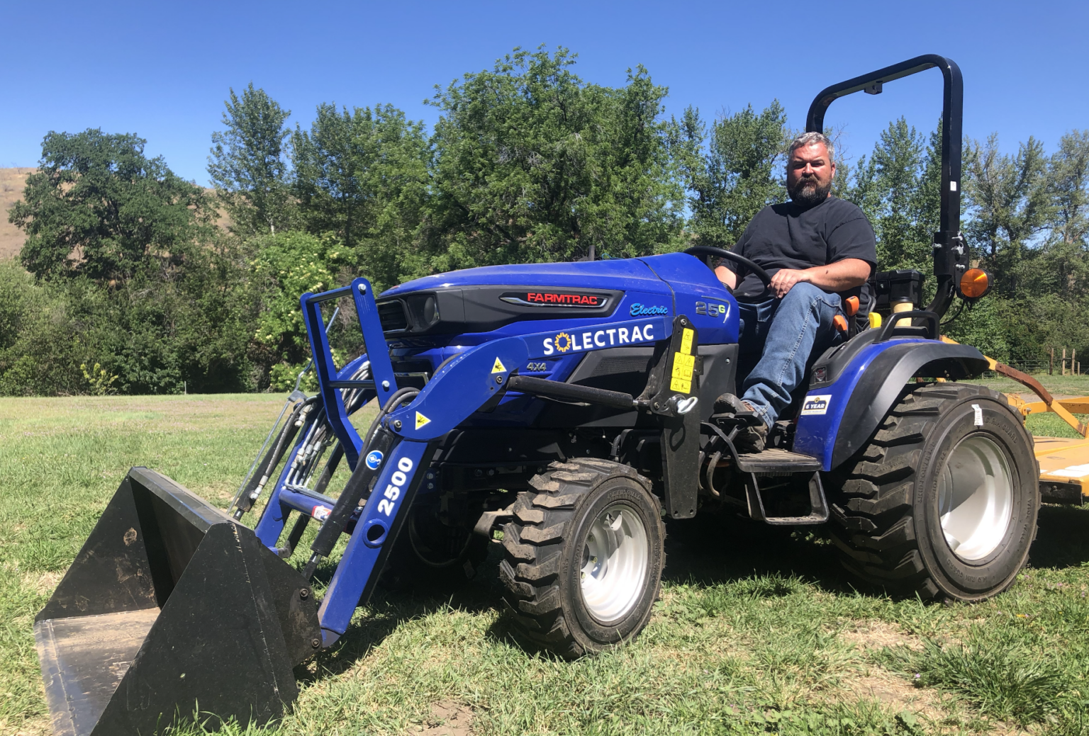 As part of a citizen science program to electrify the agricultural industry, a man at Rusted Gate Farm evaluates the performance of a blue Soléctrac electric tractor.