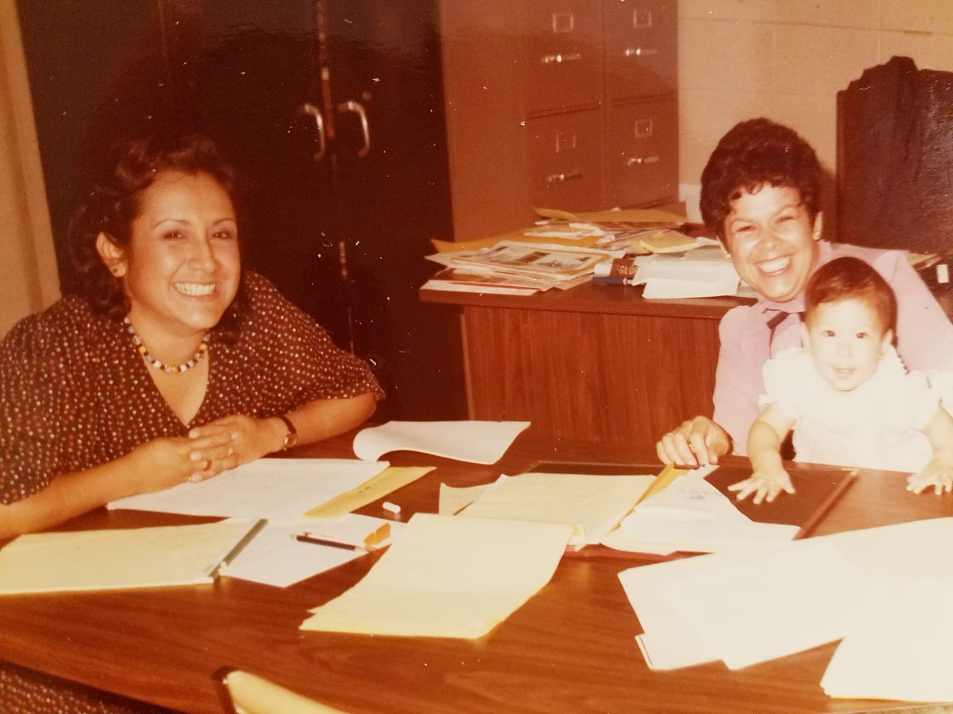  Gloria sitting with her best friend and second Vice President of AVANCE, Carmen Cortez. Carmen was a PTE Graduate and godmother to Gloria's daughter, Vanessa. She worked at AVANCE from 1976 -1990. This picture shows them writing a proposal to keep A