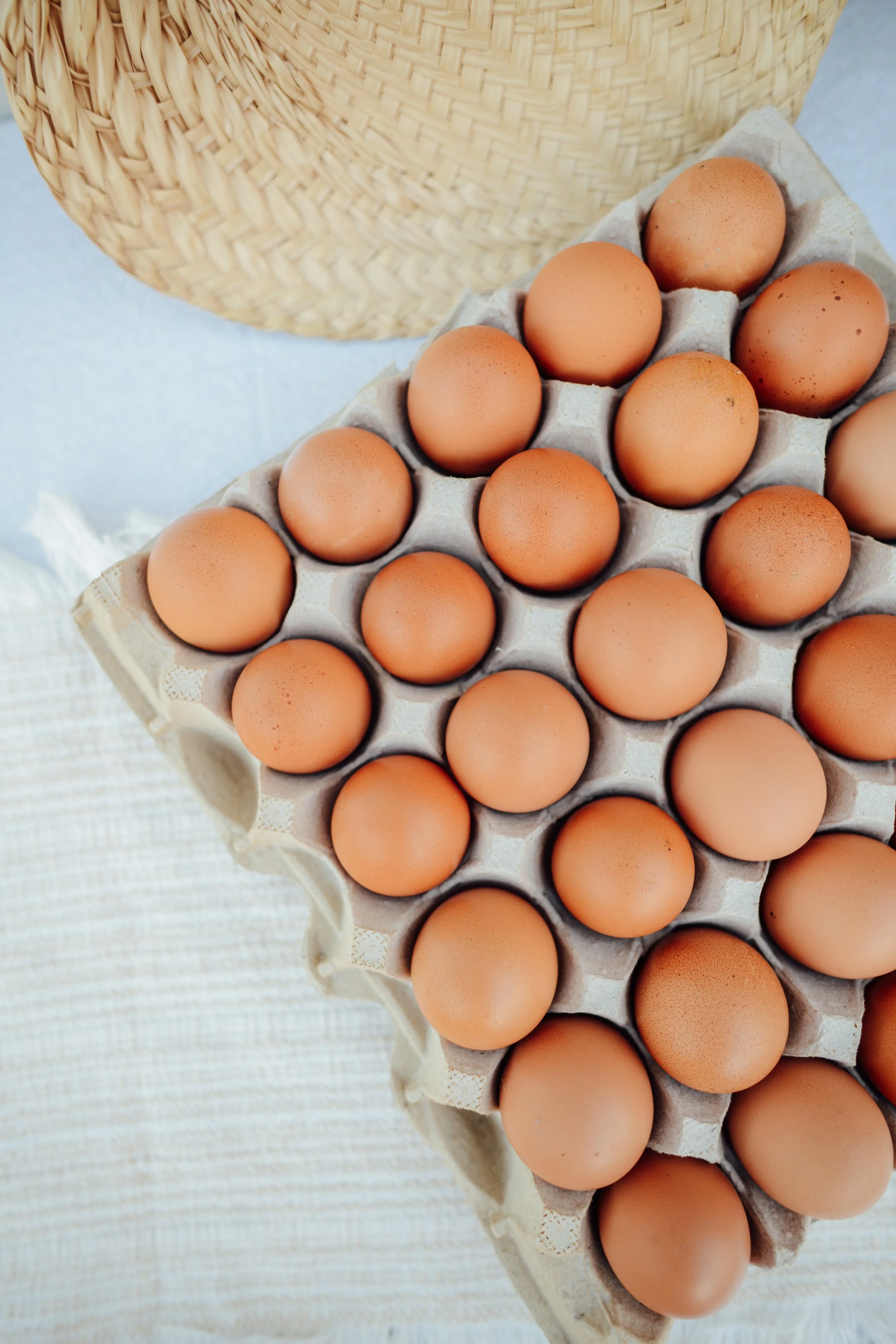 A carton of brown eggs on a white textured surface with a woven basket in the background.