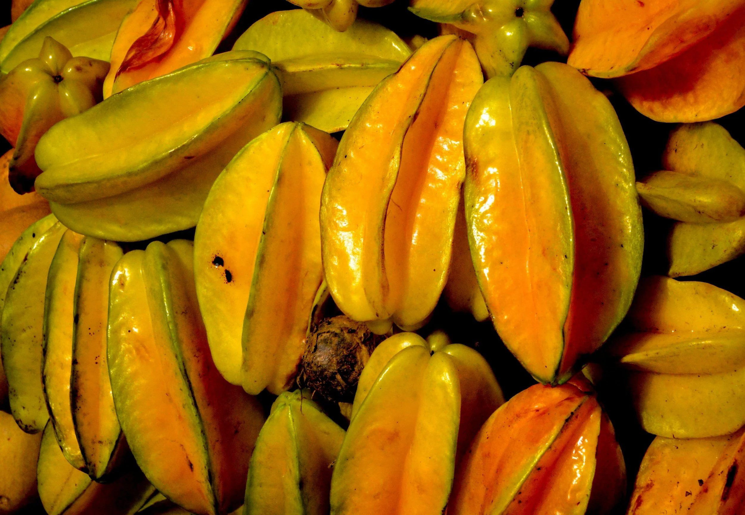 Close-up of starfruit, also known as carambola, with yellowish-green skin, some with hints of orange, arranged in a pile.