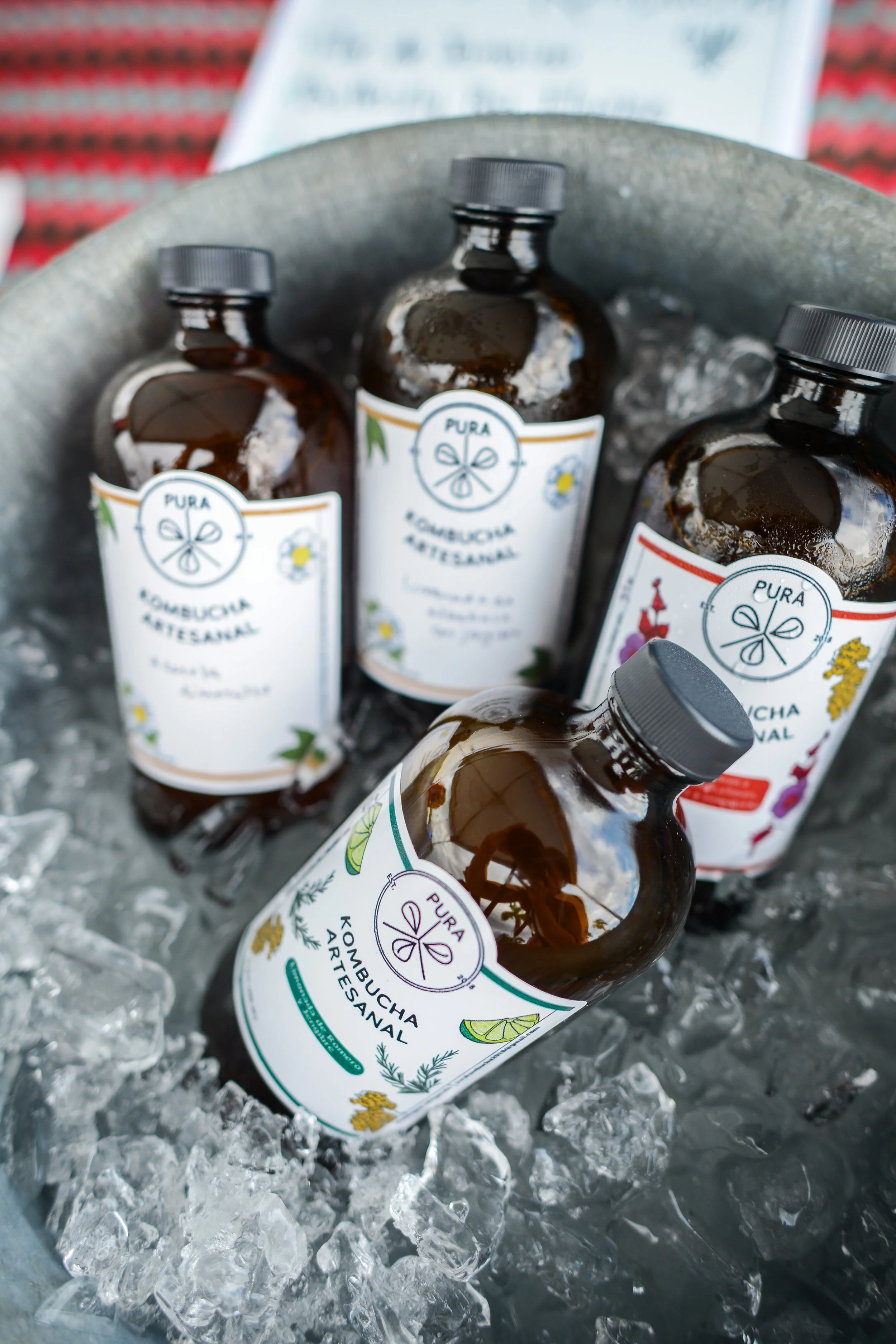 Several brown glass bottles with white labels featuring green, yellow, and purple designs, sitting in ice.